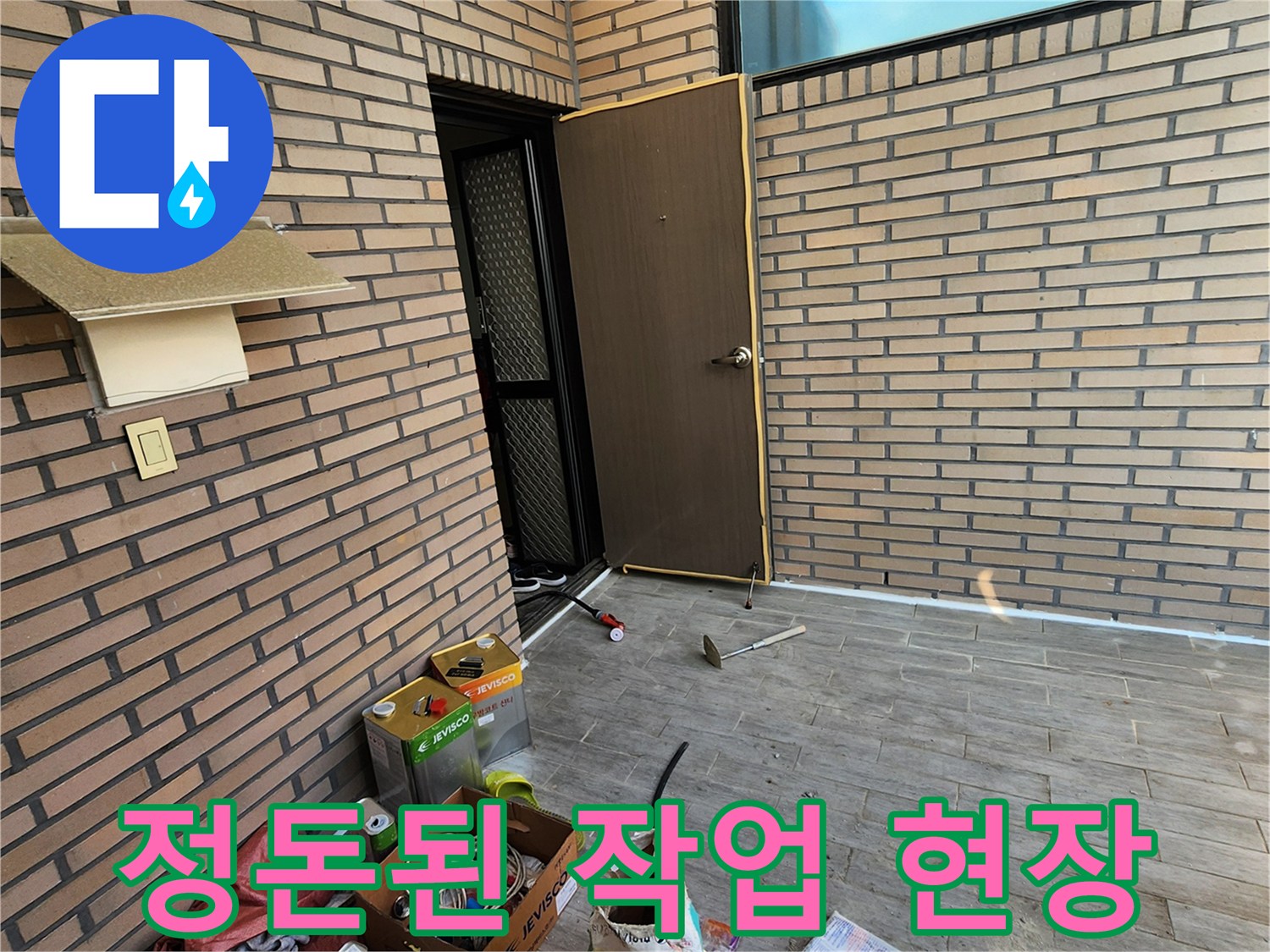 벽돌 벽면 아래에 놓인 배관 수리용 자재와 도구들입니다.