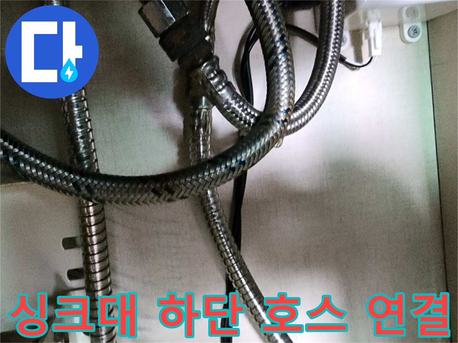 주방 싱크대 아래쪽의 꼬인 스테인식 배관과 검은색 전선 부위