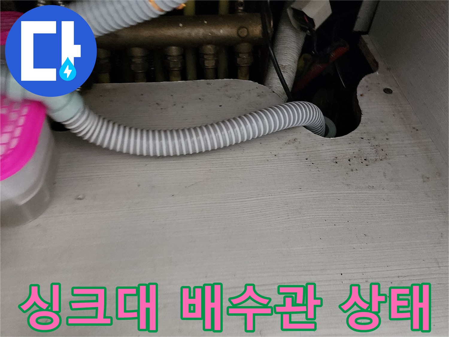 주방 싱크대 아래쪽의 굴곡진 회색 주름관과 배관 연결 부위 모습