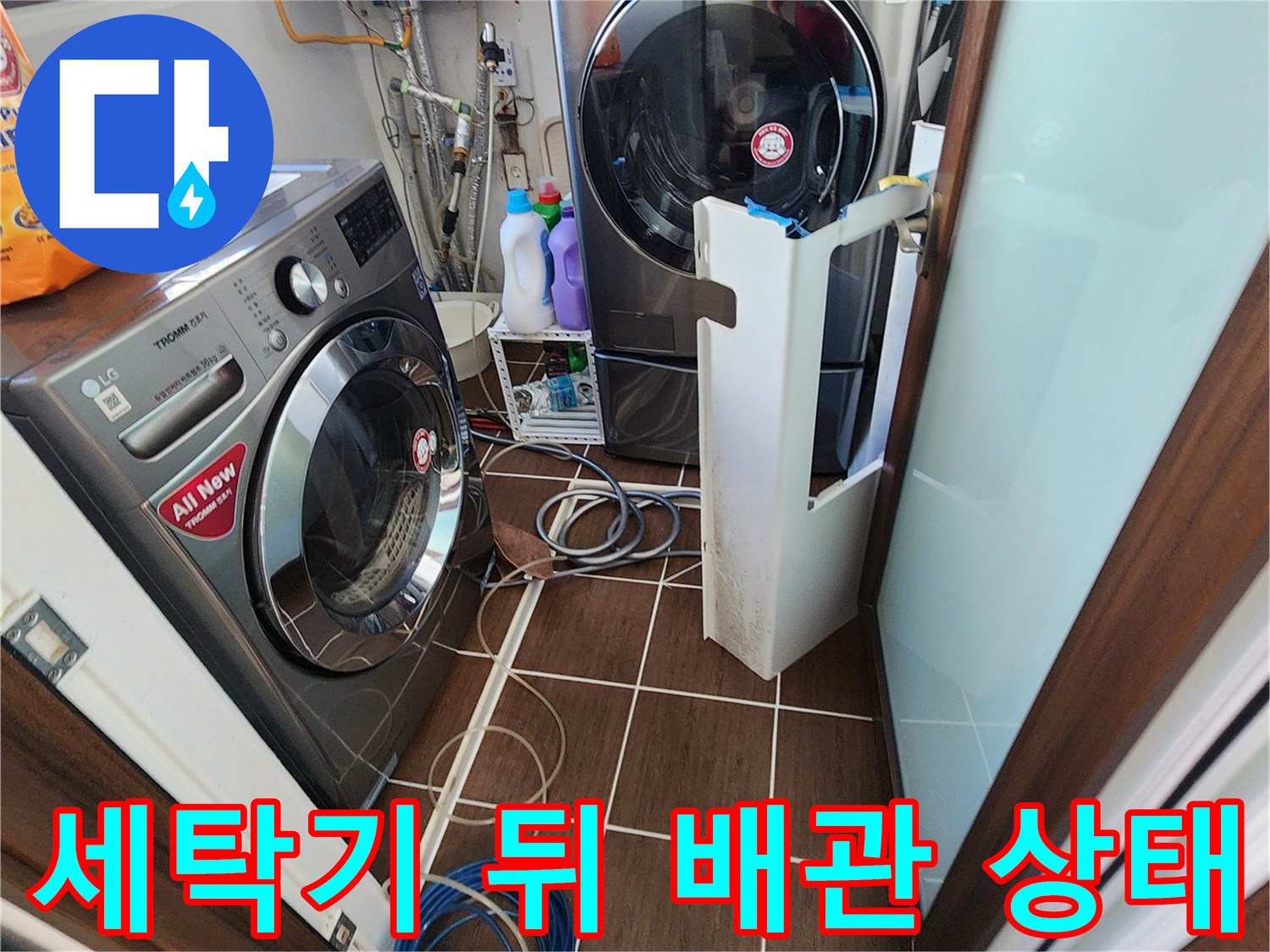 세탁기와 건조기 하단부의 배관 연결 부위 및 바닥 타일 모습입니다.
