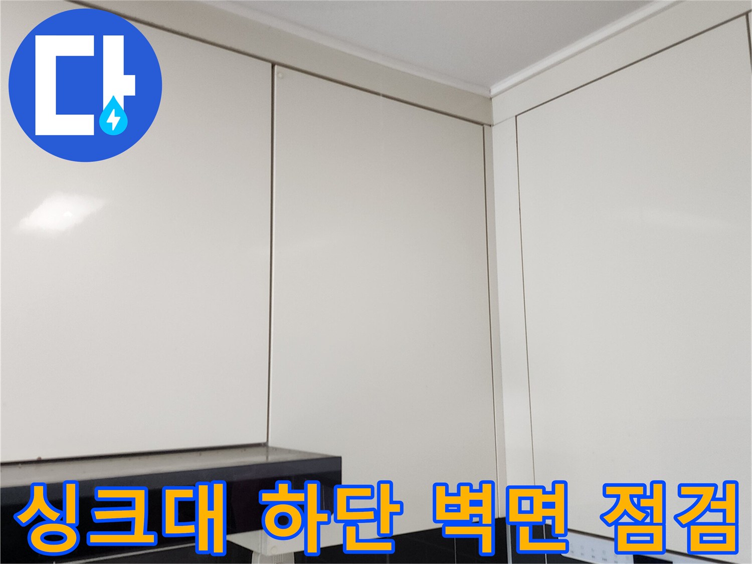 흰색 상부장 아래 검은색 타일 벽면을 촬영한 사진입니다.
