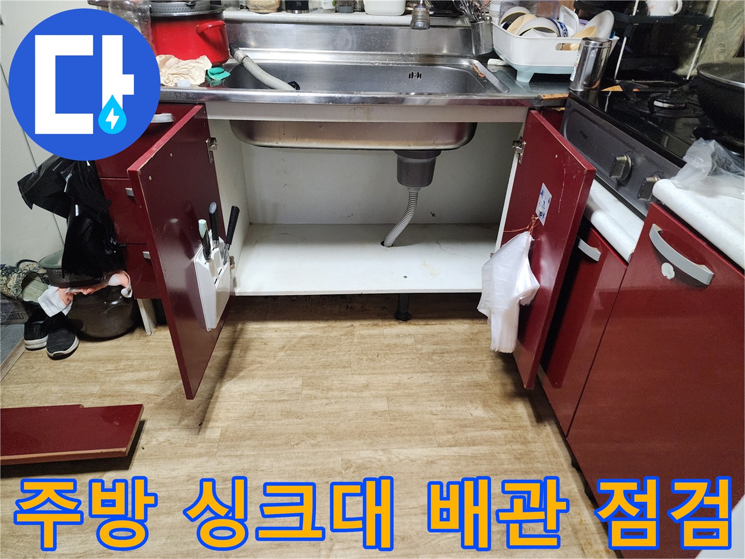 싱크대 하부장 내부의 배수 호스와 바닥 면 상태를 촬영한 사진입니다.