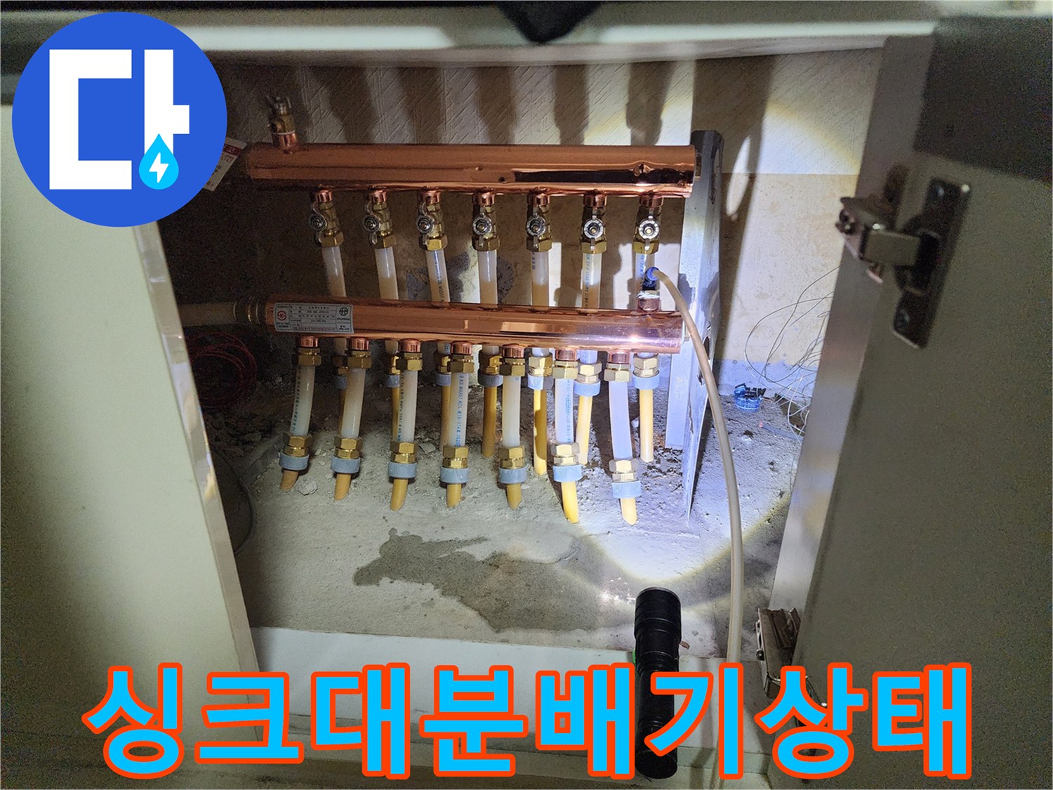 싱크대 하부장 내부의 구리 소재 난방 분배기와 연결 배관 모습
