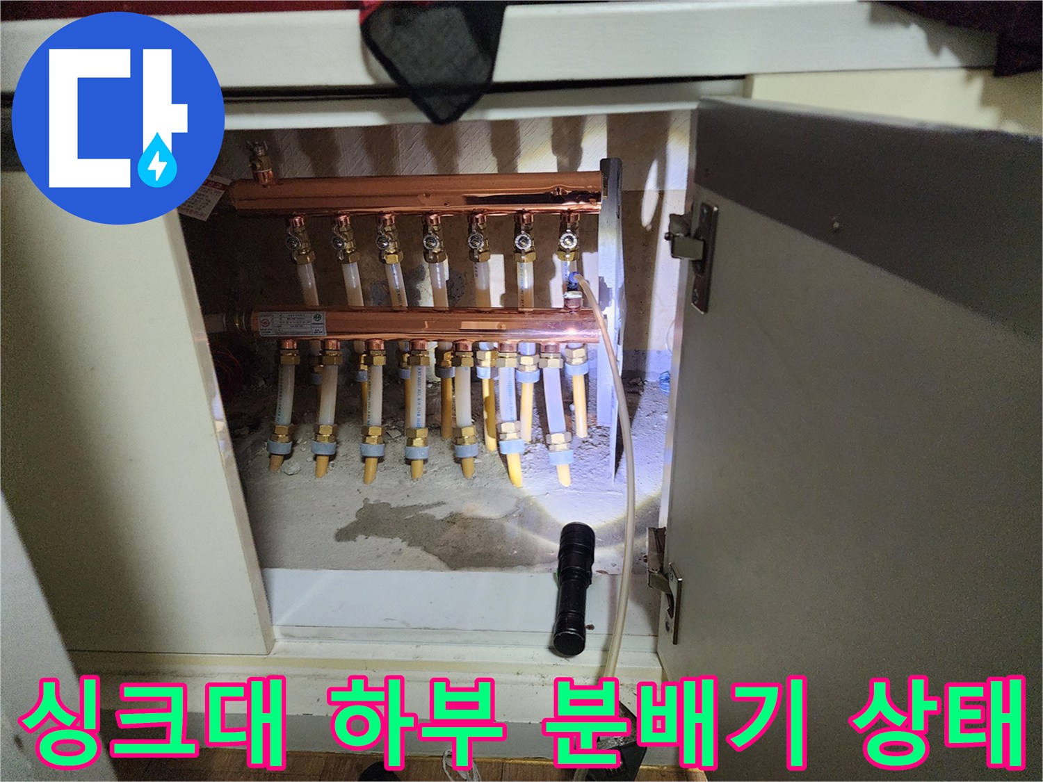 싱크대 하부장에 노출된 난방 분배기와 연결 배관 모습
