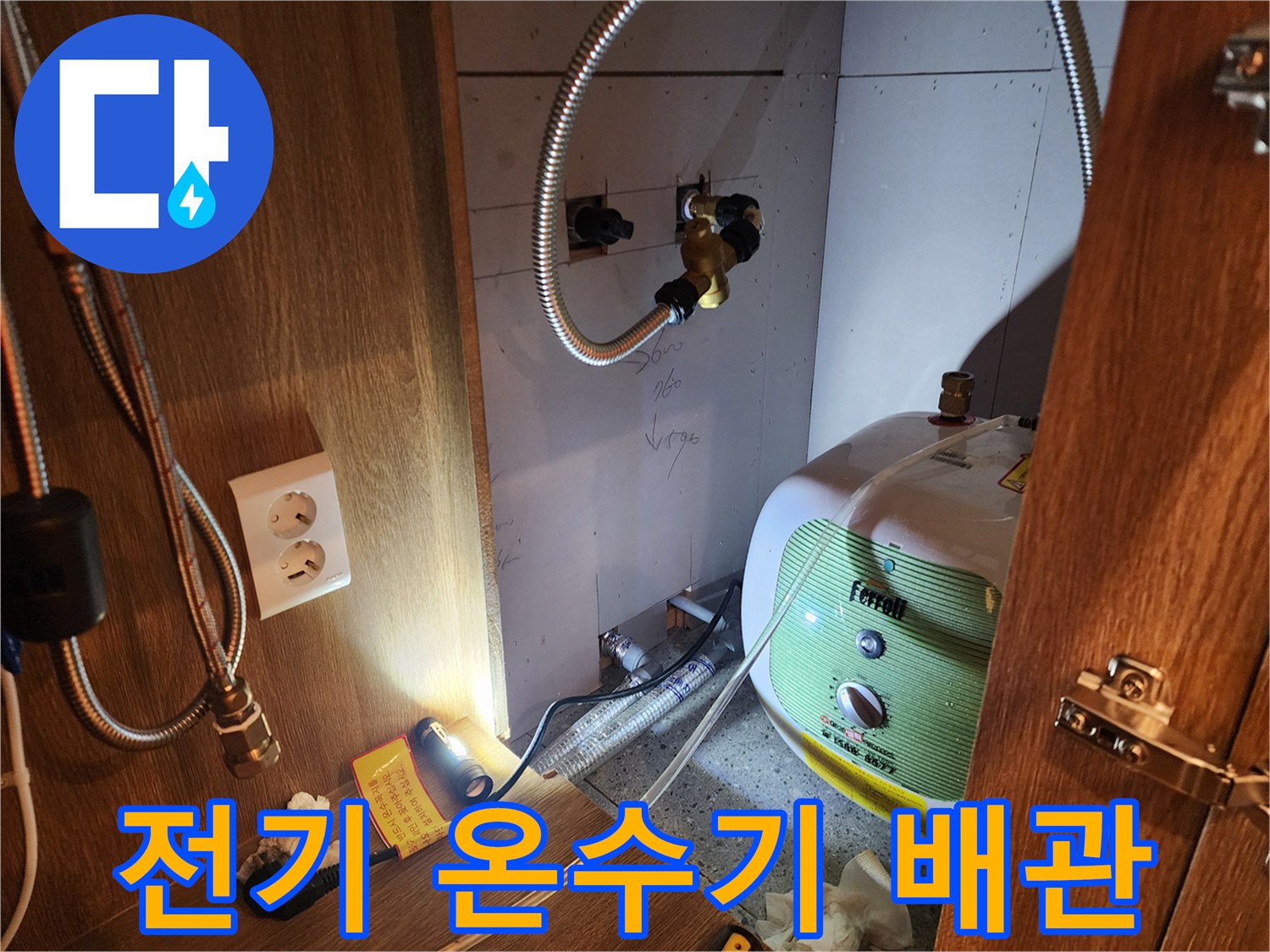 주방 싱크대 아래 설치된 전기 온수기와 금속 연결 호스 촬영