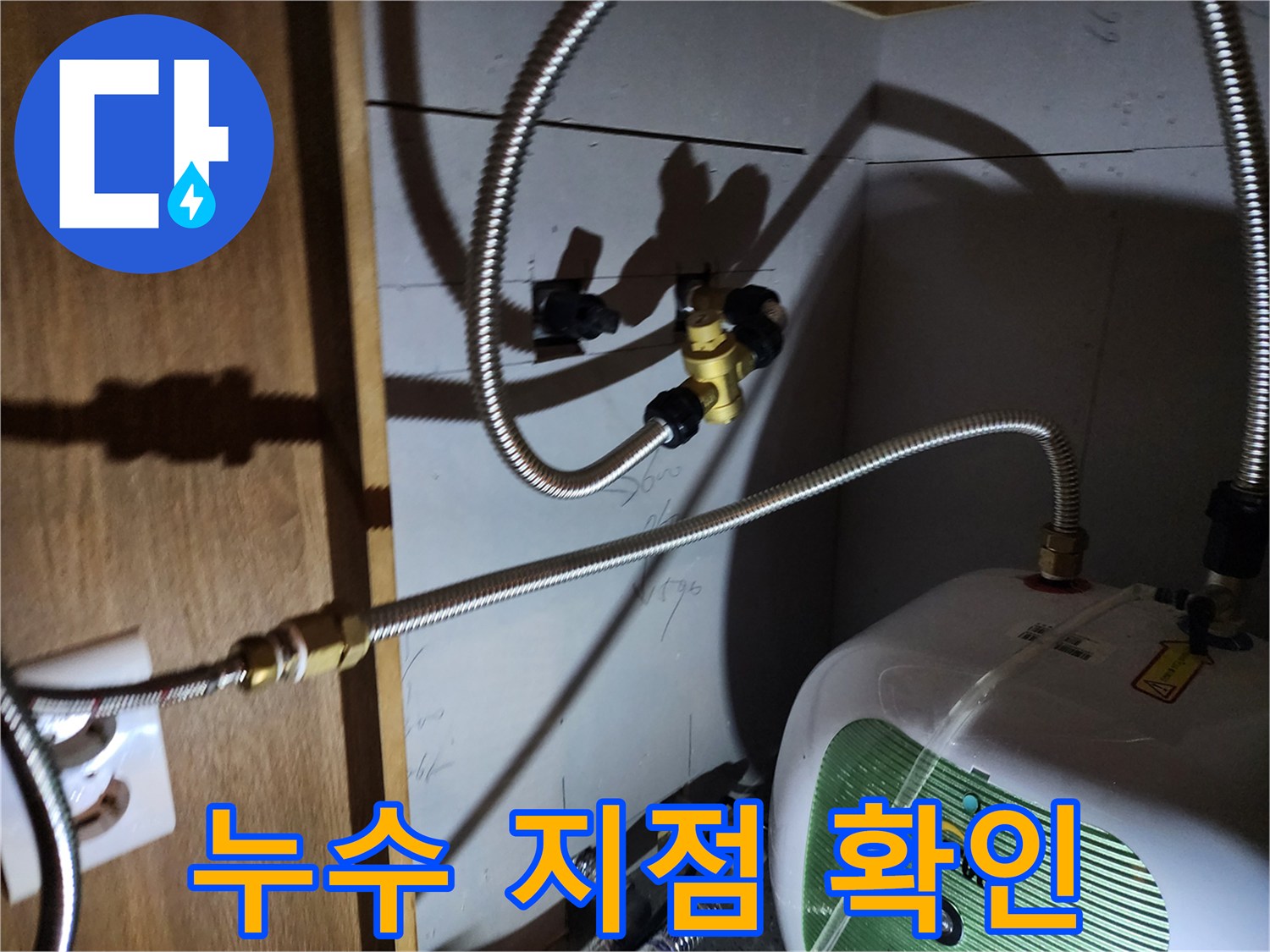 주방 하부장 내 전기 온수기와 연결된 금속 호스의 누수 부위 근접 촬영