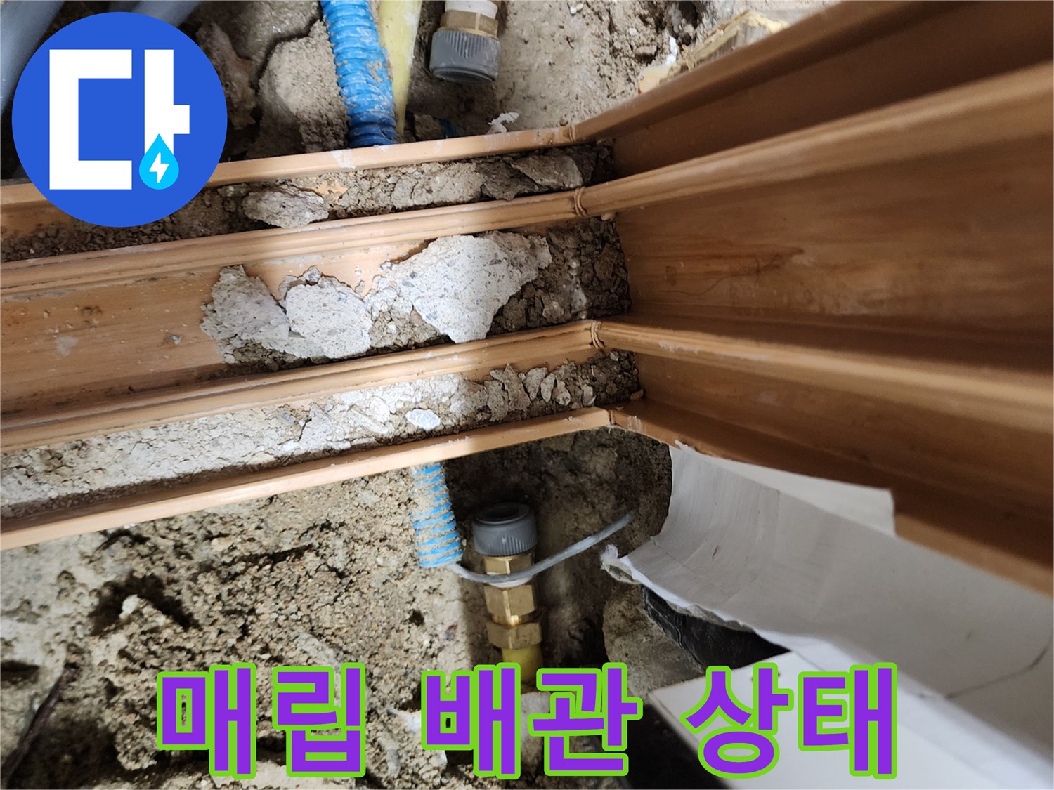 흙과 콘크리트 사이로 드러난 파란색 및 노란색 수도 배관