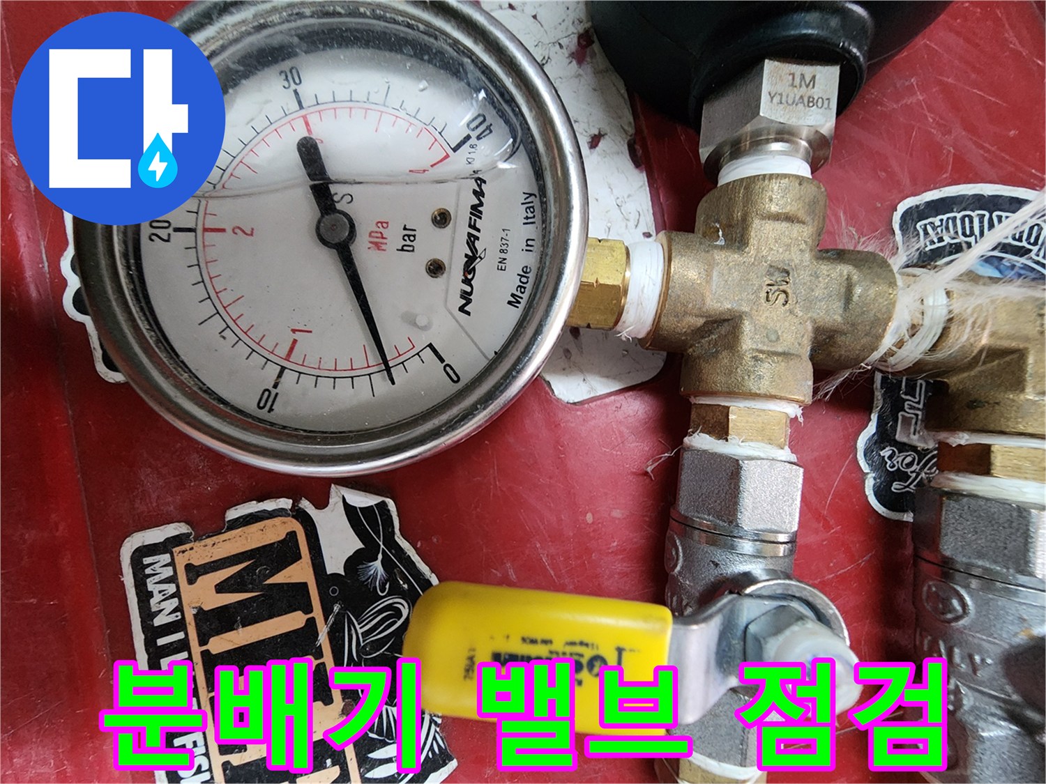 노란색 손잡이가 달린 분배기 밸브와 압력계의 모습입니다.