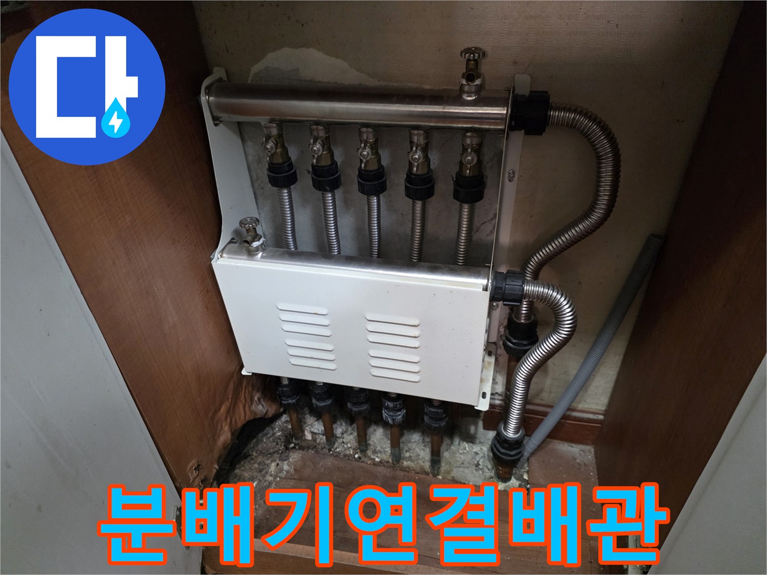 싱크대 아래 보일러 분배기와 연결된 은색 주름관의 모습입니다.