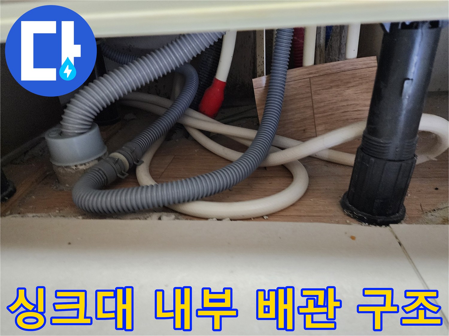 복잡하게 얽힌 싱크대 하부의 회색 주름관과 흰색 호스 배열