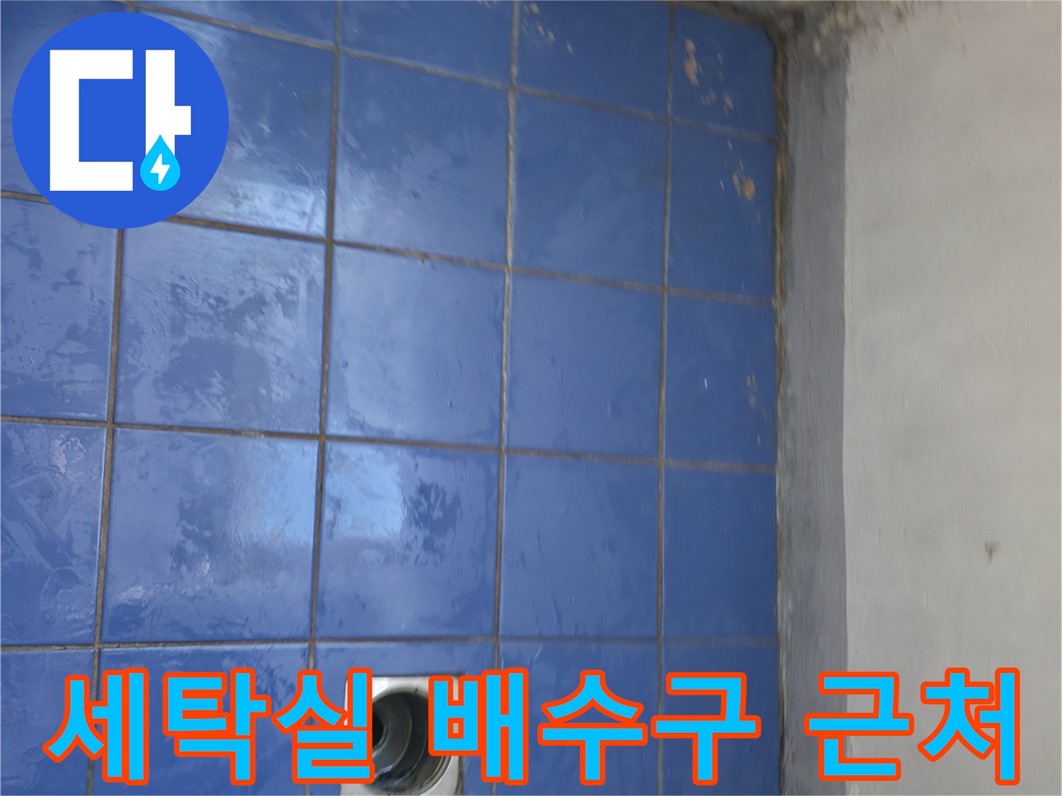 파란 타일 바닥에 위치한 세탁실 배수구 입구 모습입니다.