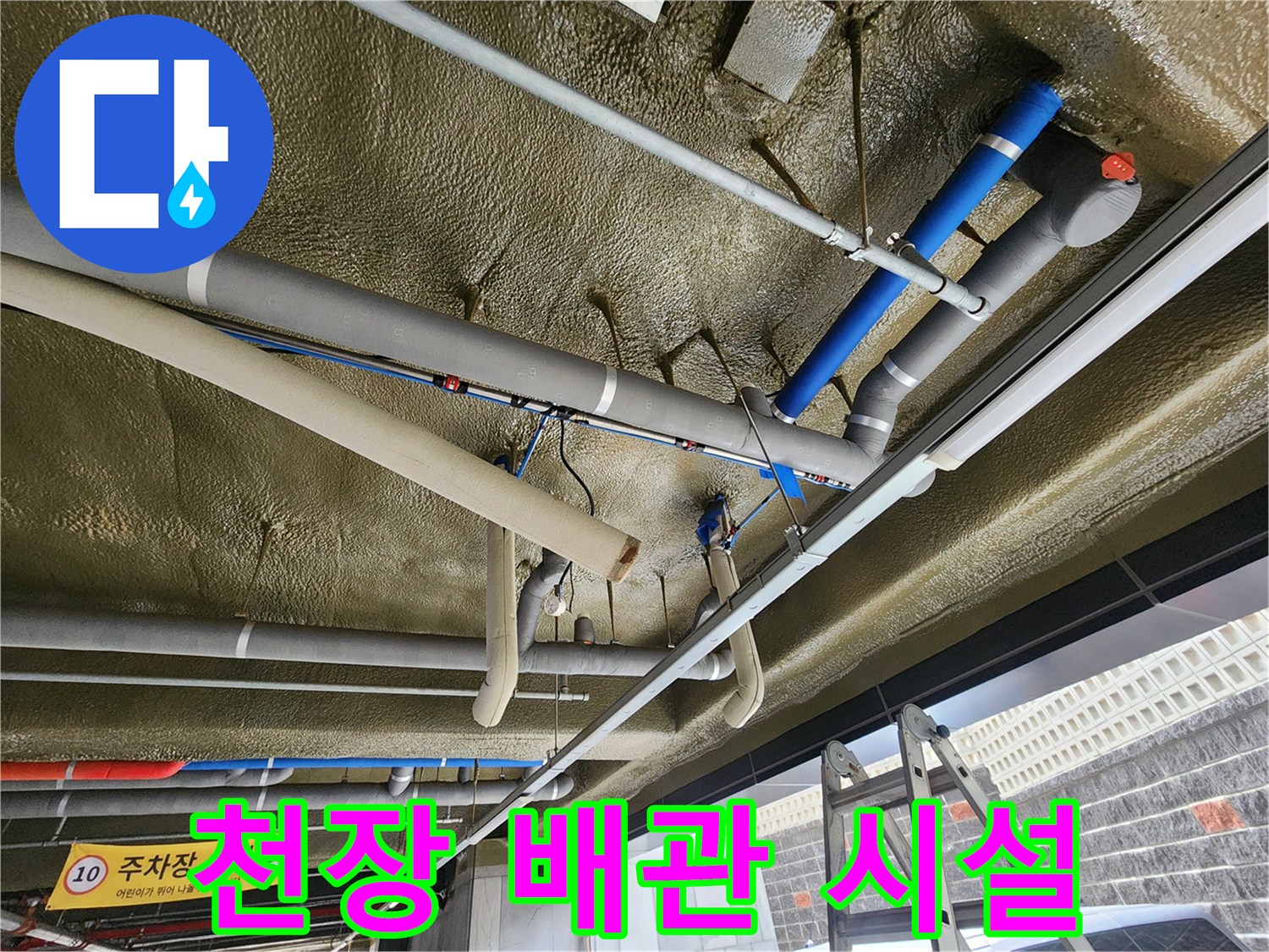 지하 주차장 천장에 복잡하게 배치된 은색 및 파란색 배관 시스템
