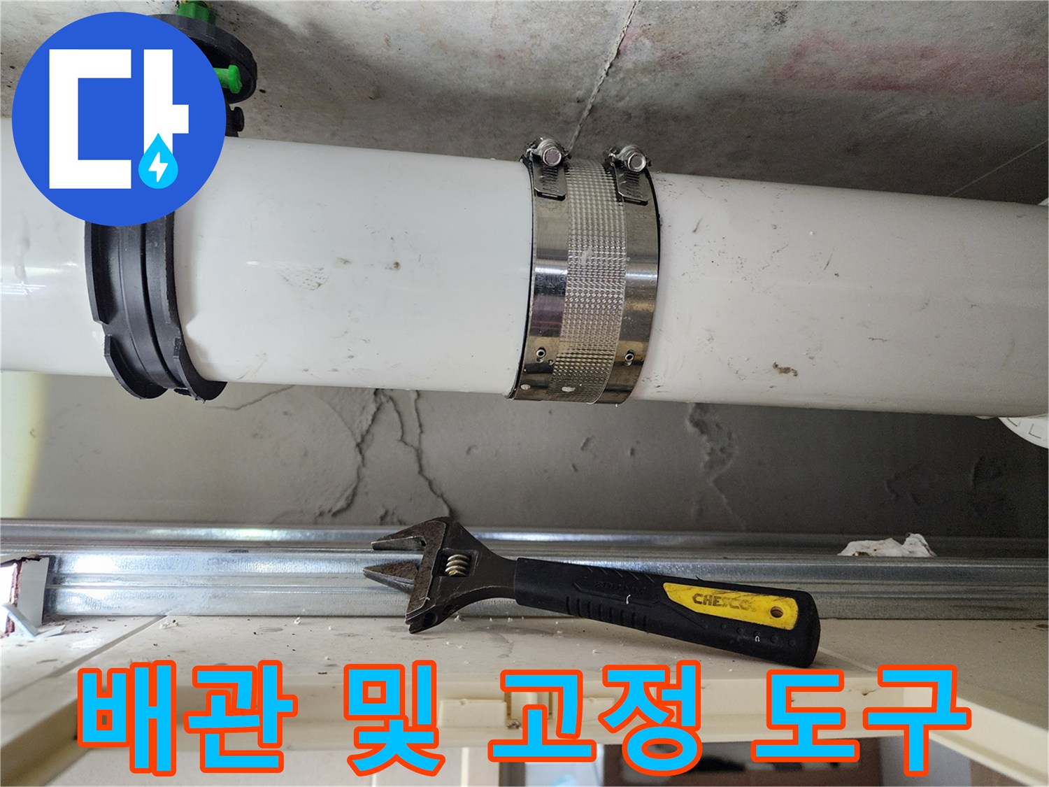 흰색 배관과 조임용 밴드 그리고 아래에 놓인 몽키 스패너