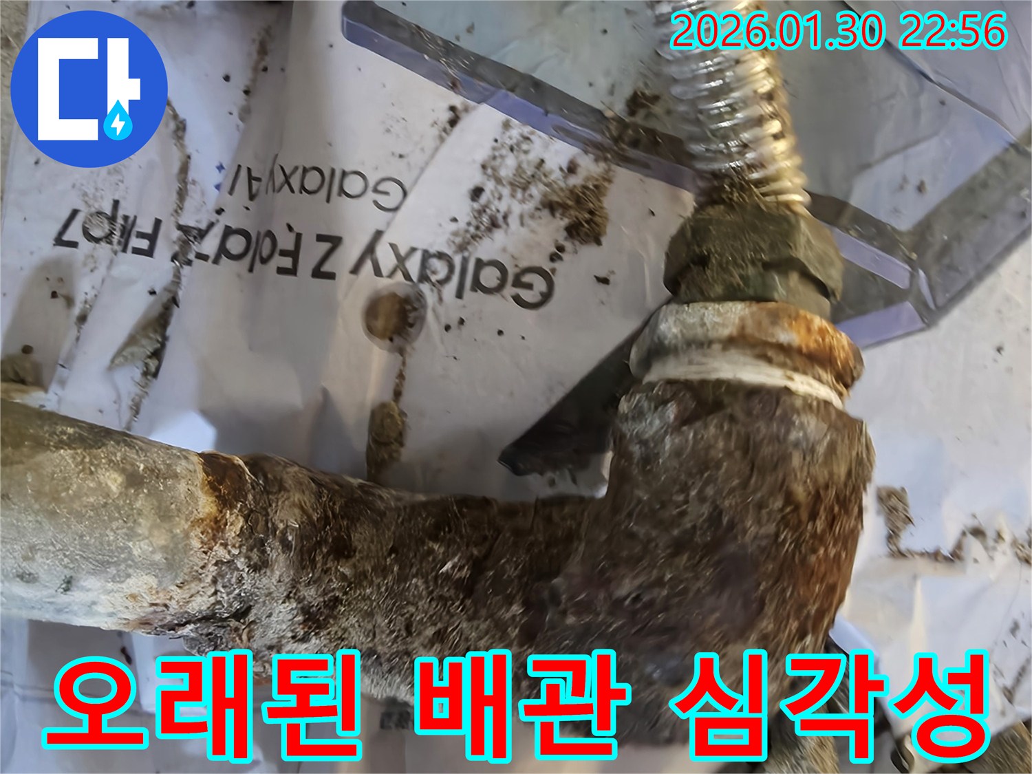 심하게 녹슬고 부식된 금속 배관의 엘보 연결부-누수가 발생하고 있음을 시사합니다.