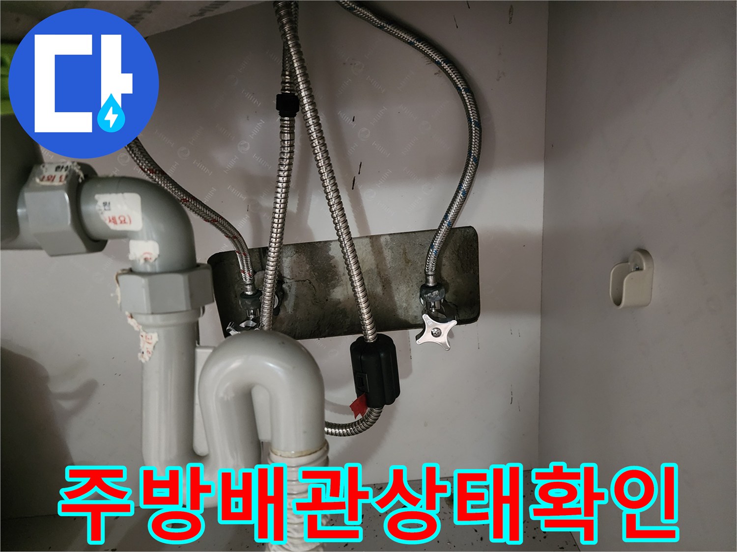 싱크대 하부장 내부의 노출된 금속 주름관과 수도 밸브 모습