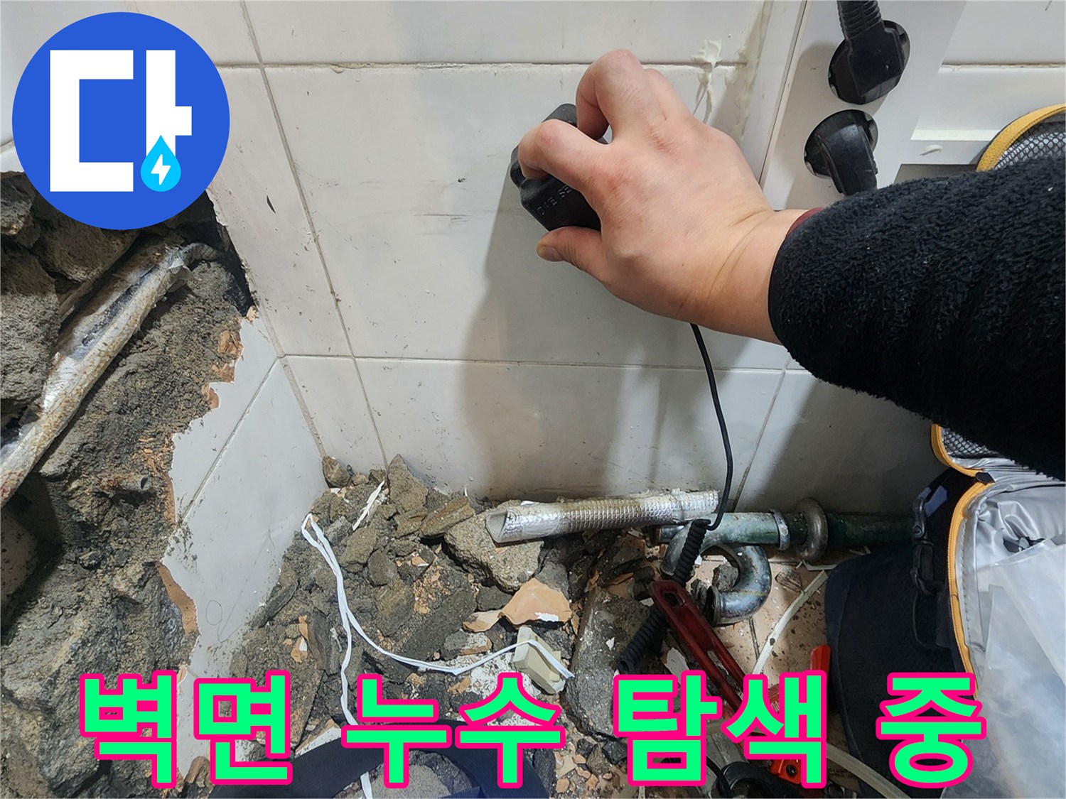 화장실 타일 벽면에 가스 탐지기를 대고 누수 지점을 찾는 장면
