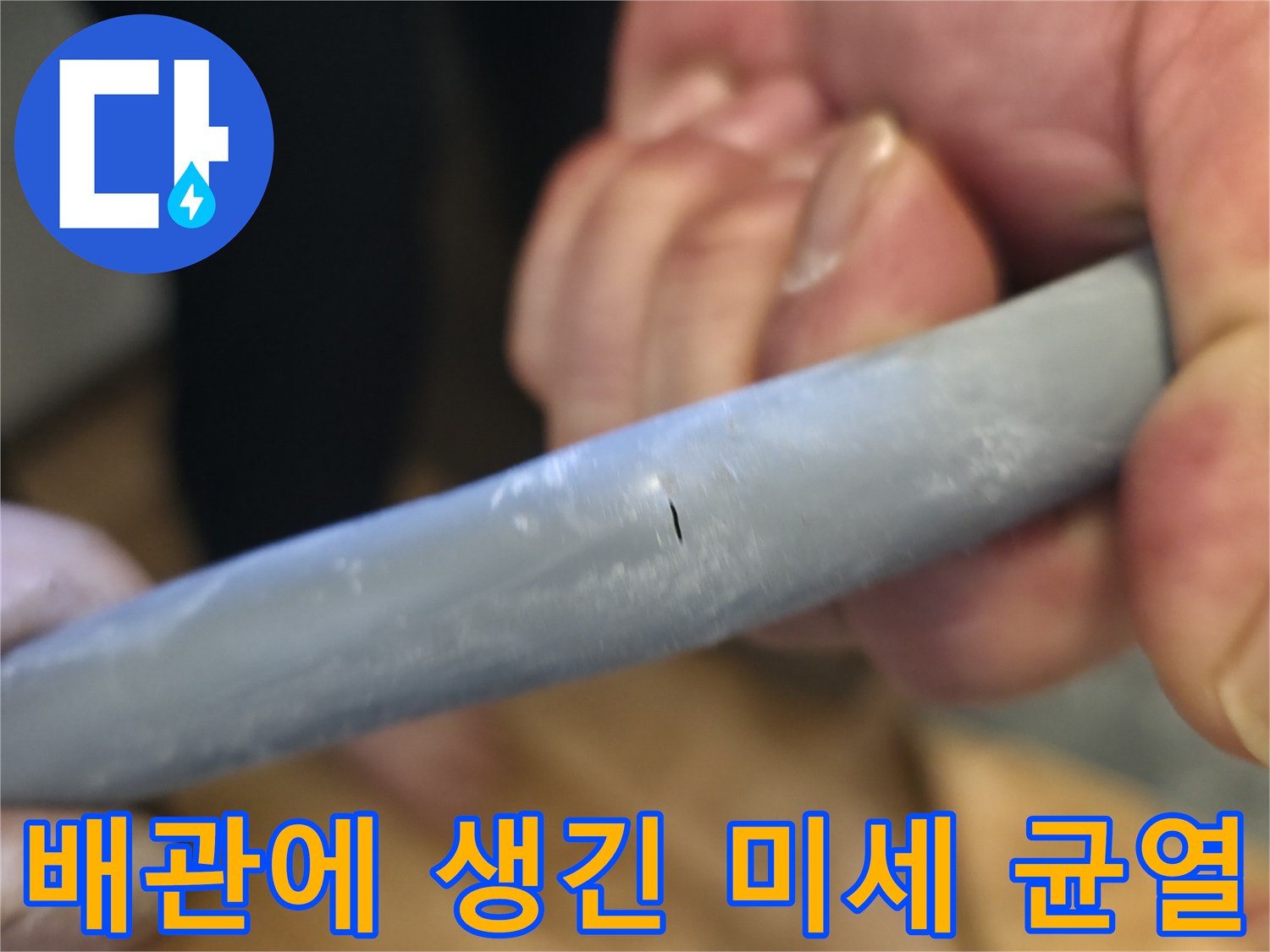 손상된 배관 부위의 작은 구멍을 손으로 가리키며 보여주는 사진