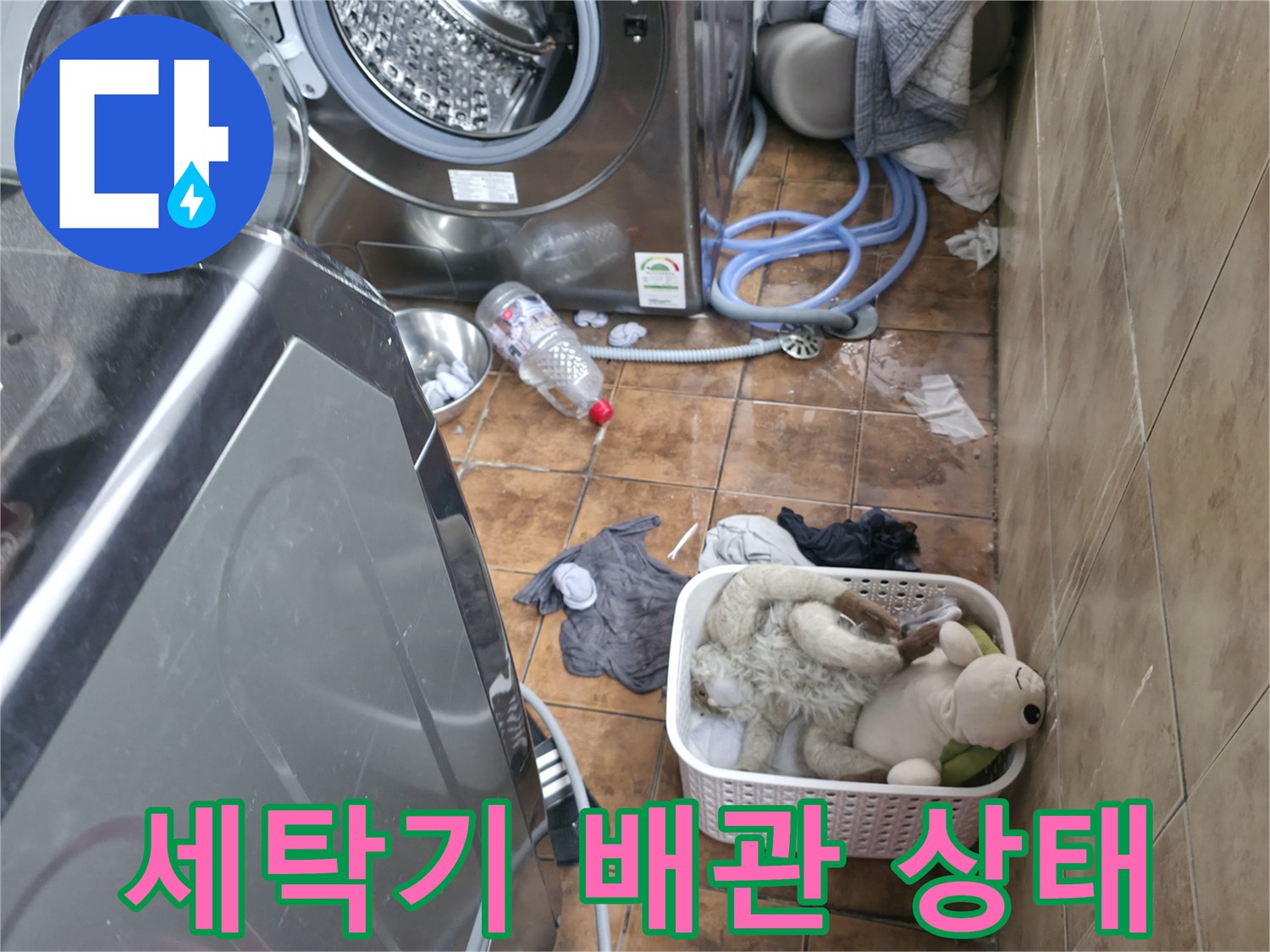 세탁기와 배수 호스 주변의 젖은 타일 바닥을 촬영한 사진입니다.