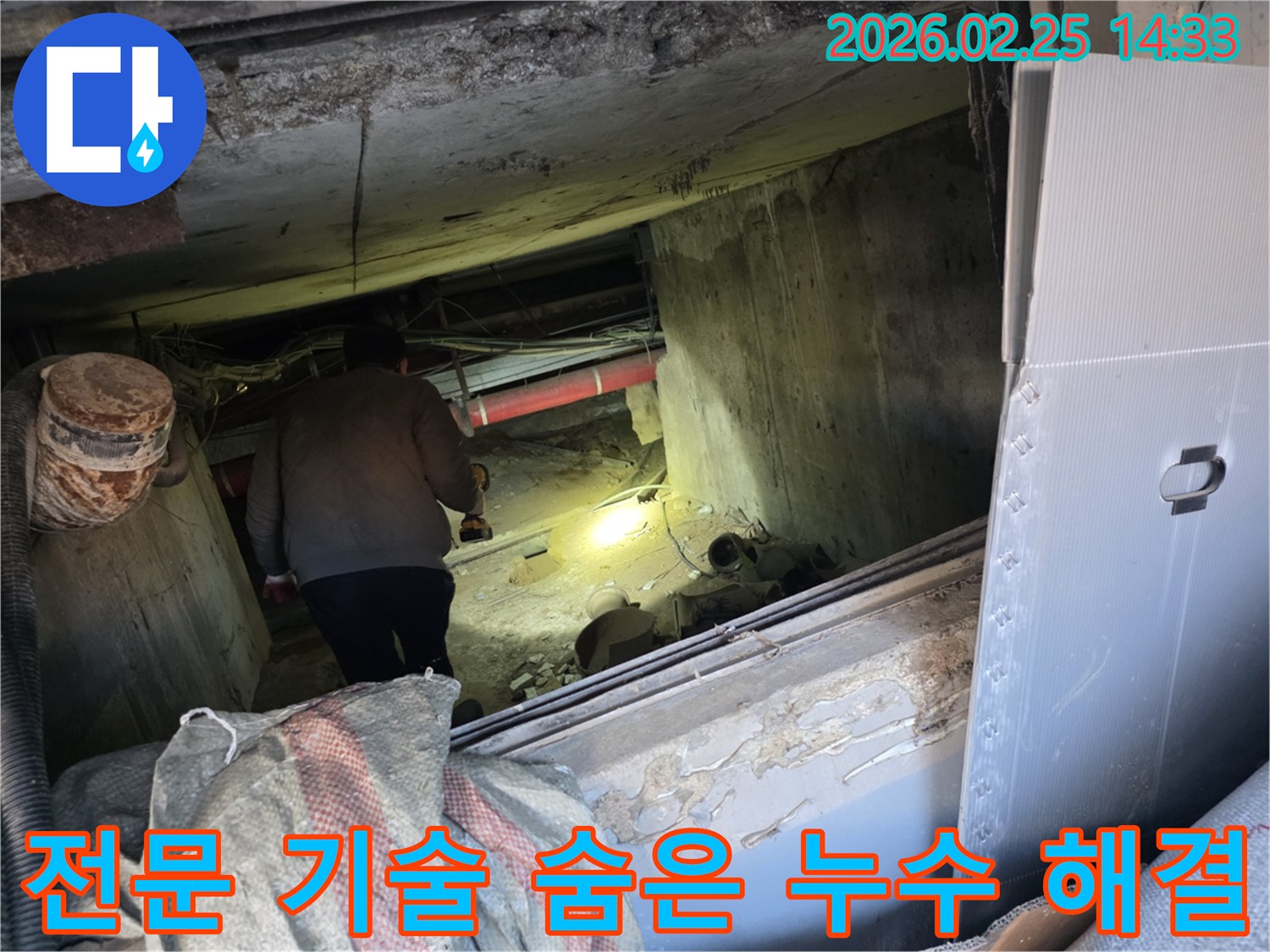 누수 전문 엔지니어가-어둡고 좁은 공간에서-손전등을 비춰가며-전문 기술을 활용하여-숨겨진 누수 문제를-해결하기 위해 탐지하는 모습입니다.