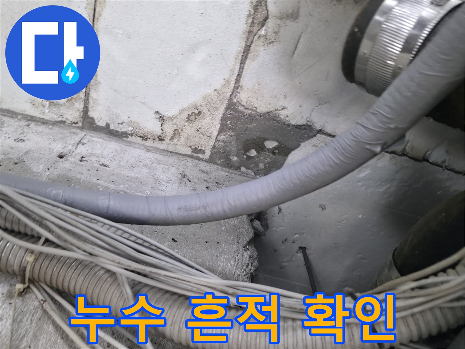 물자국이 남은 타일 벽면과 회색 배관 및 전선 뭉치