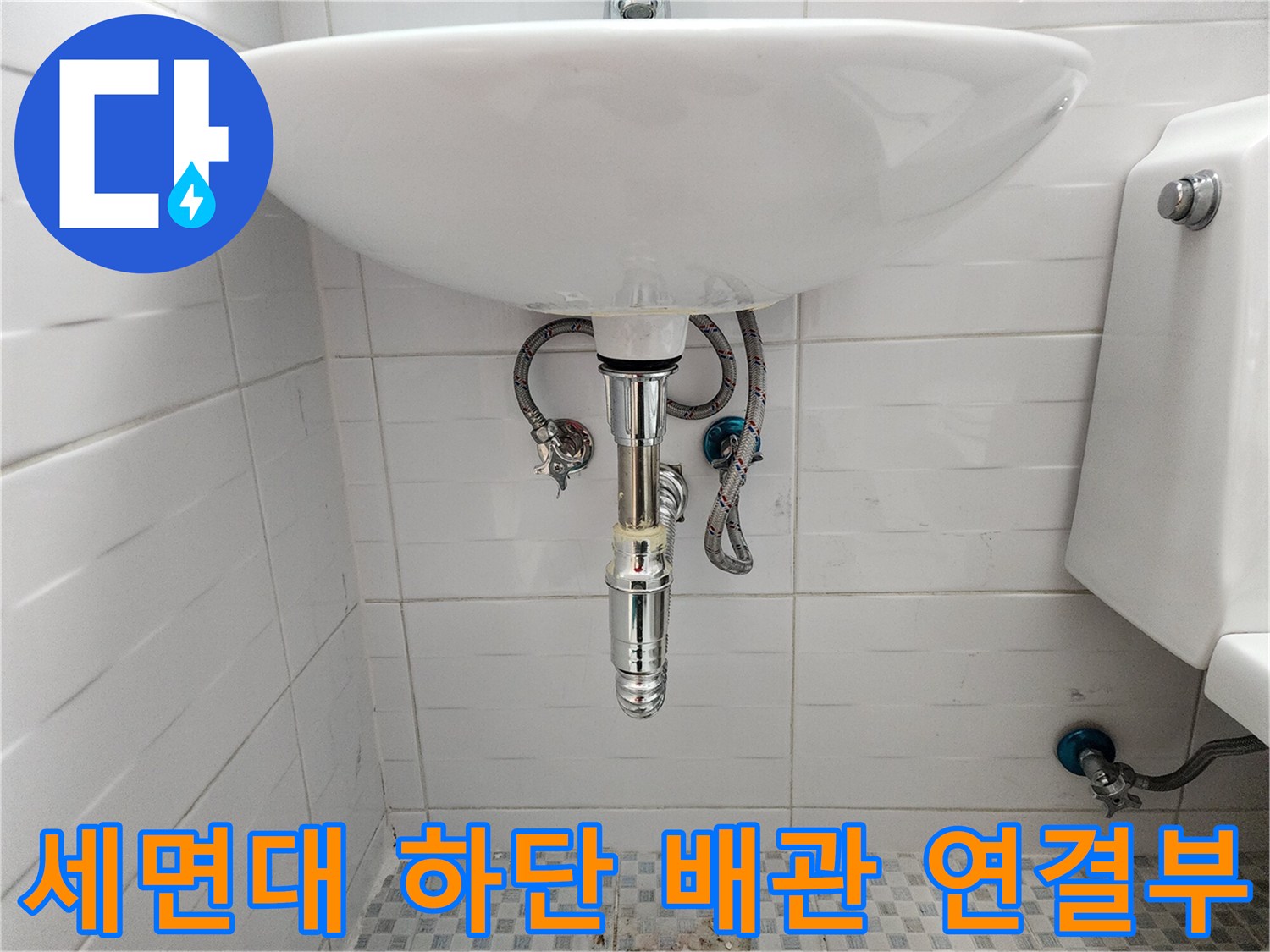 흰색 세면대 아래로 연결된 은색 금속 재질의 급수 호스 및 밸브