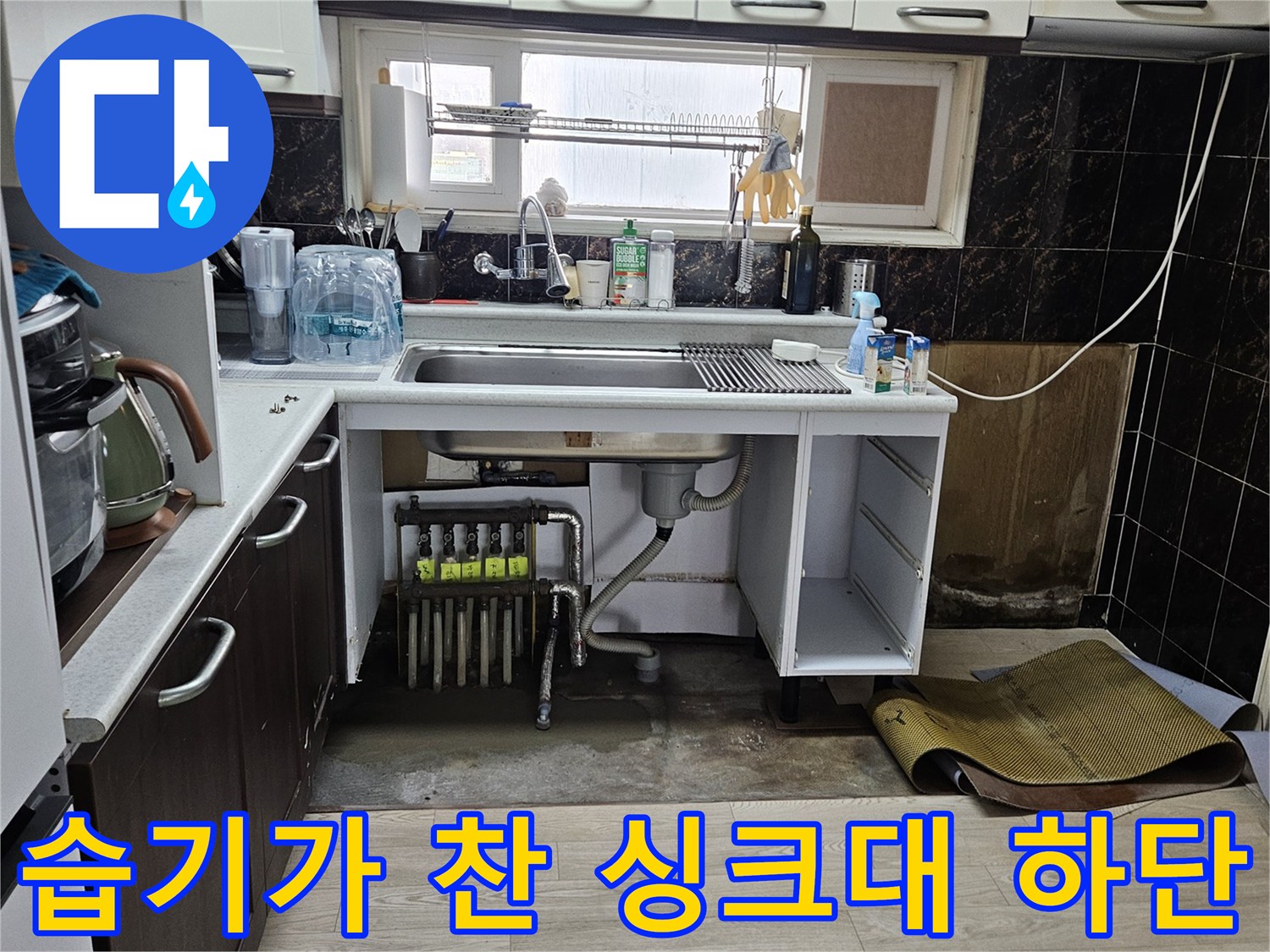 싱크대 아래 공간-분배기 주변의 젖은 바닥과 노출된 배관 연결 부위