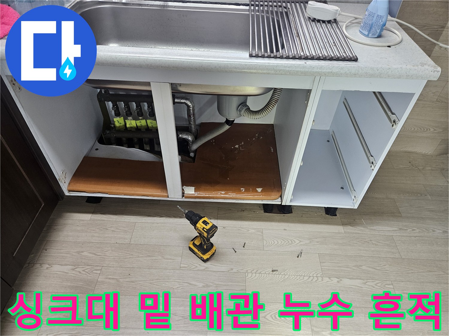 싱크대 아래 분배기 주변의 젖은 바닥과 노출된 배관 구조