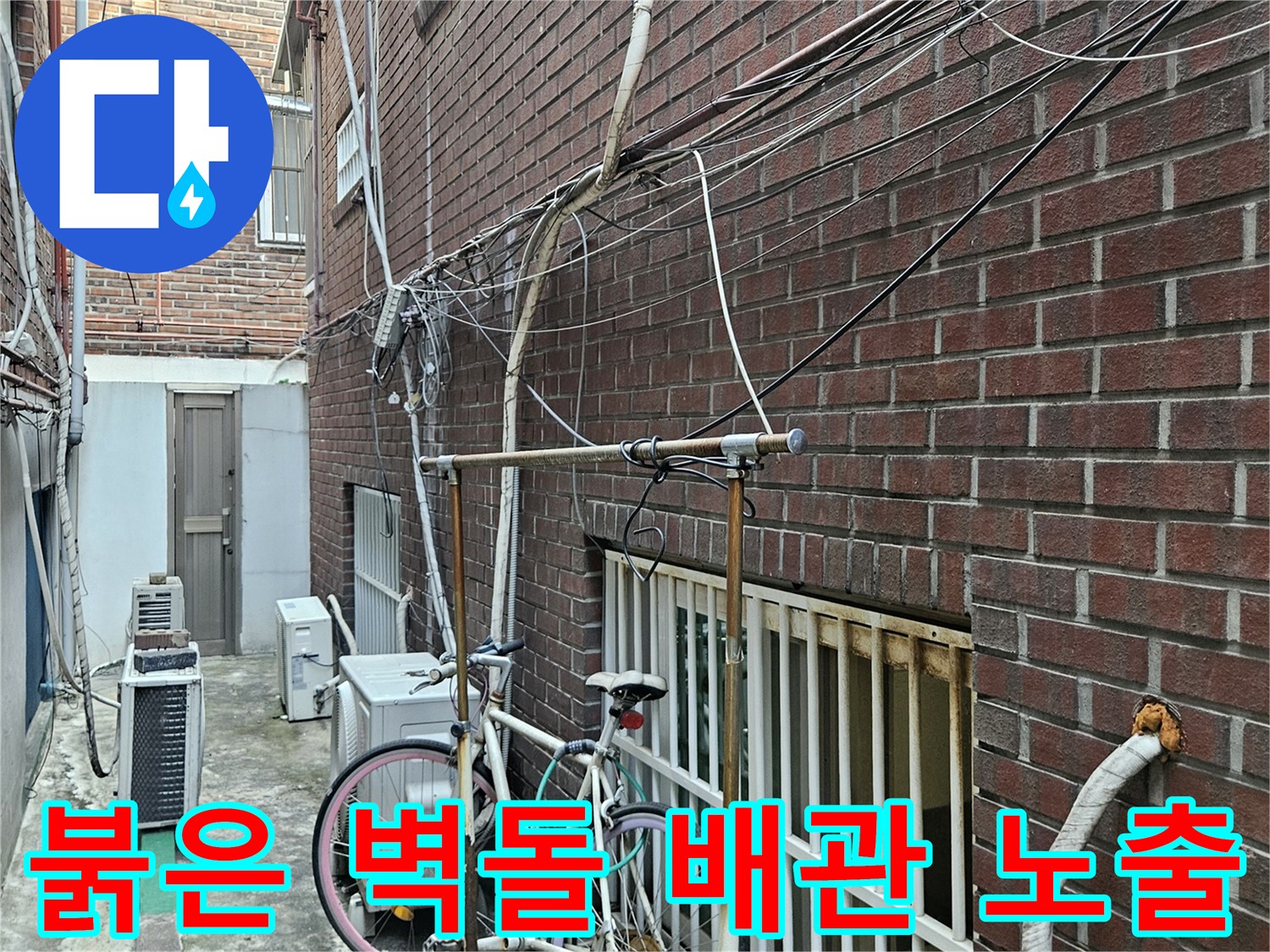 붉은색 벽돌 외벽에 설치된 다양한 배관 라인과 실외기 주변 모습