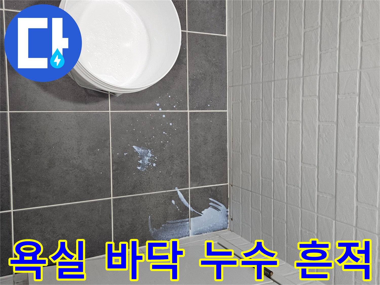 물기가 묻어있는 어두운 색상의 욕실 타일과 양동이