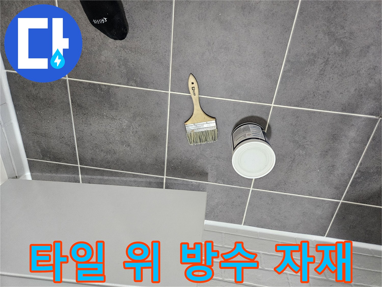 어두운 회색 타일 위에 놓인 흰 통과 붓