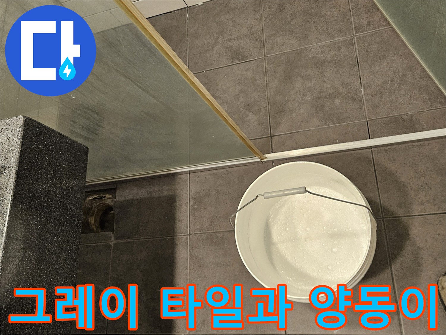 어두운 회색 타일 위-하얀색 물통이 놓인 화장실 전경