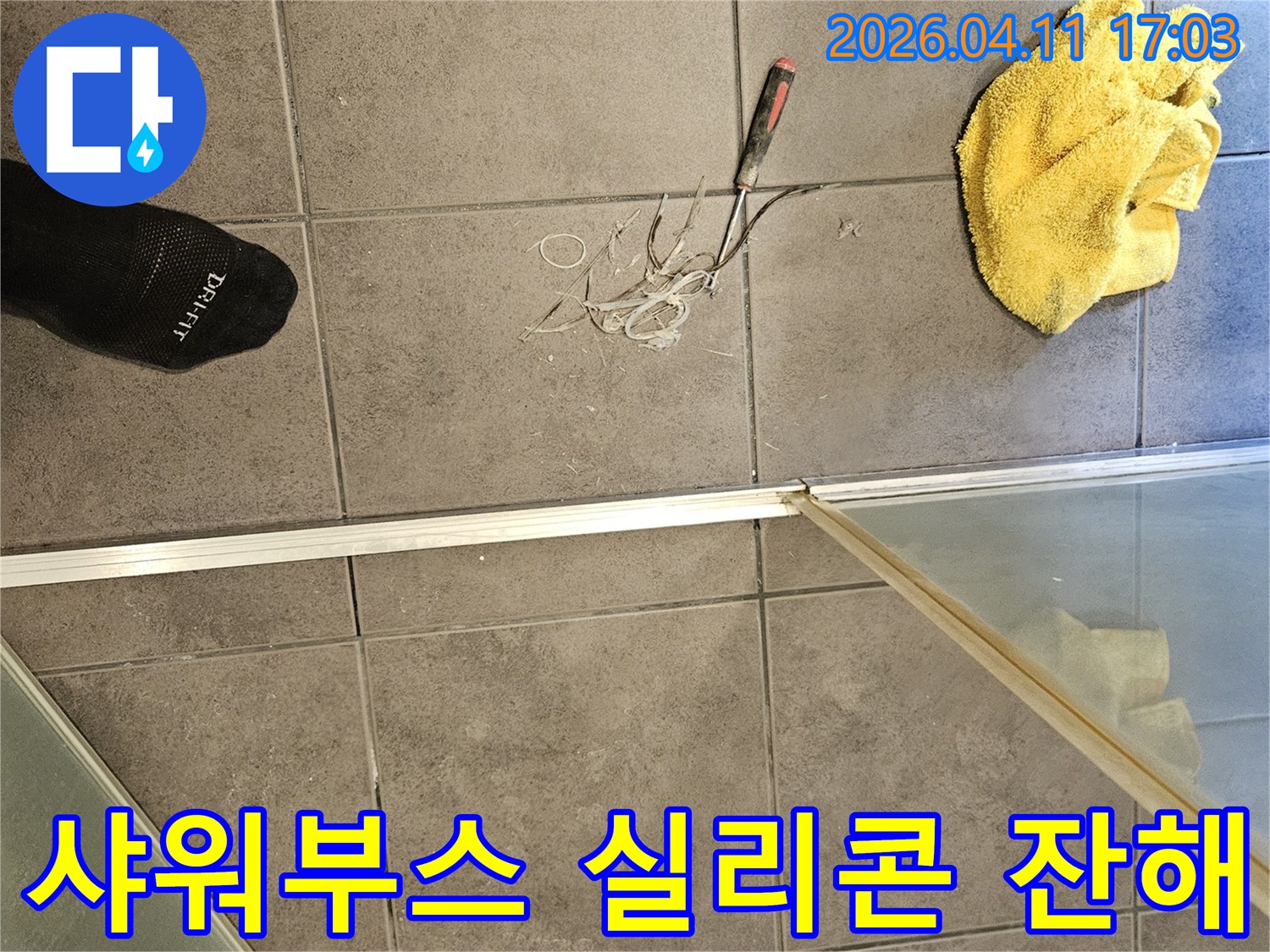 욕실 바닥 타일 위-노란 수건과 공구-그리고 샤워부스에서 제거된 실리콘 잔해물들