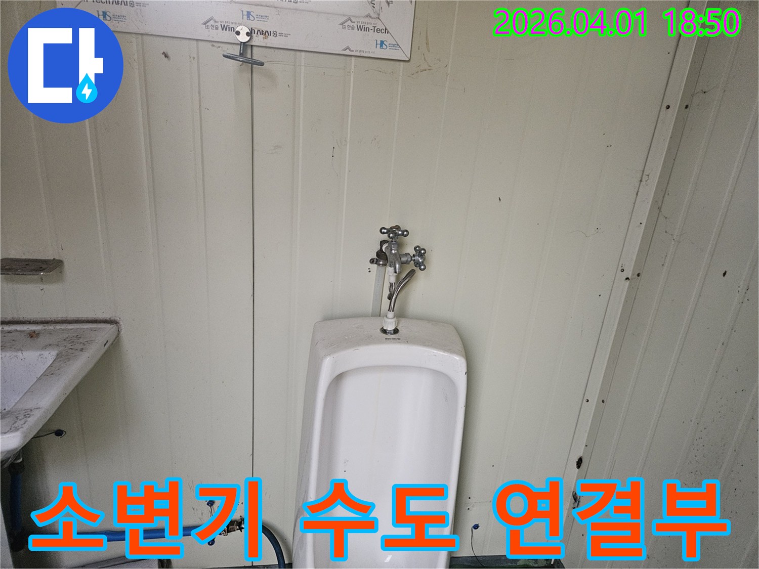 가설 건축물 내 소변기 상단에 설치된 수도꼭지와-하단 급수 호스 연결 밸브의-전반적인 상태를 보여주는 이미지