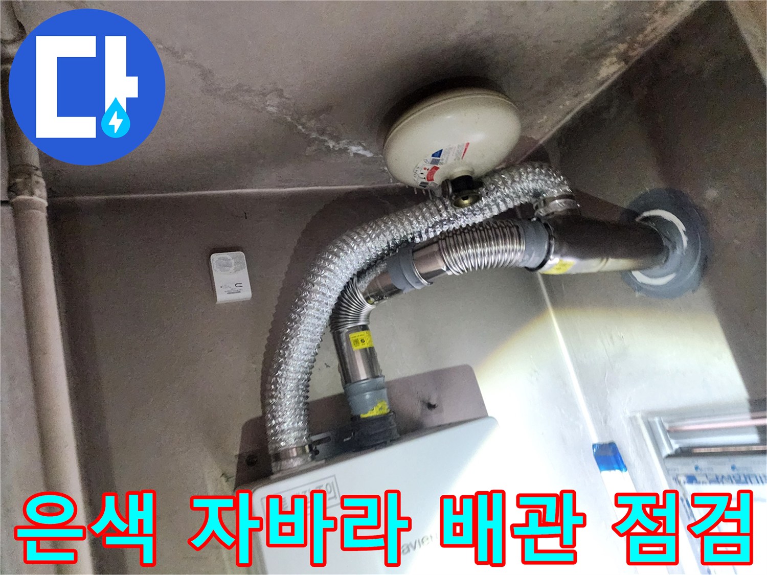 천장에 연결된 은색 주름관과 둥근 환기구 시설물입니다.