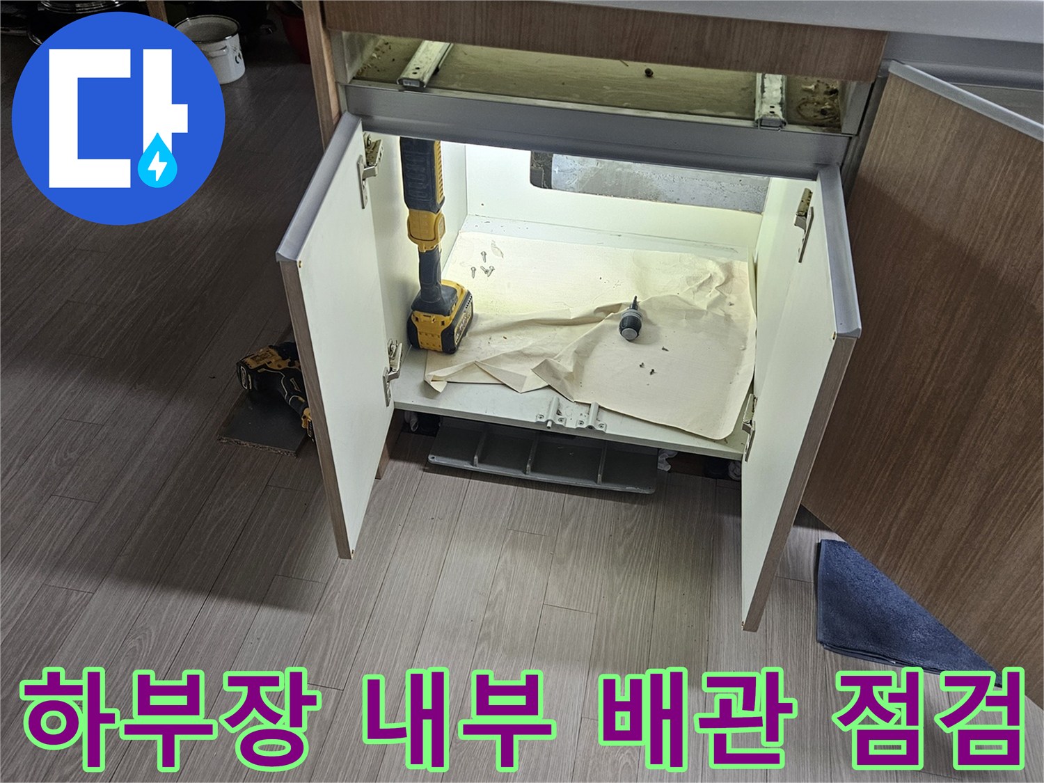 배관 보수를 위해 싱크대 하부장을 열고 작업 중인 장면