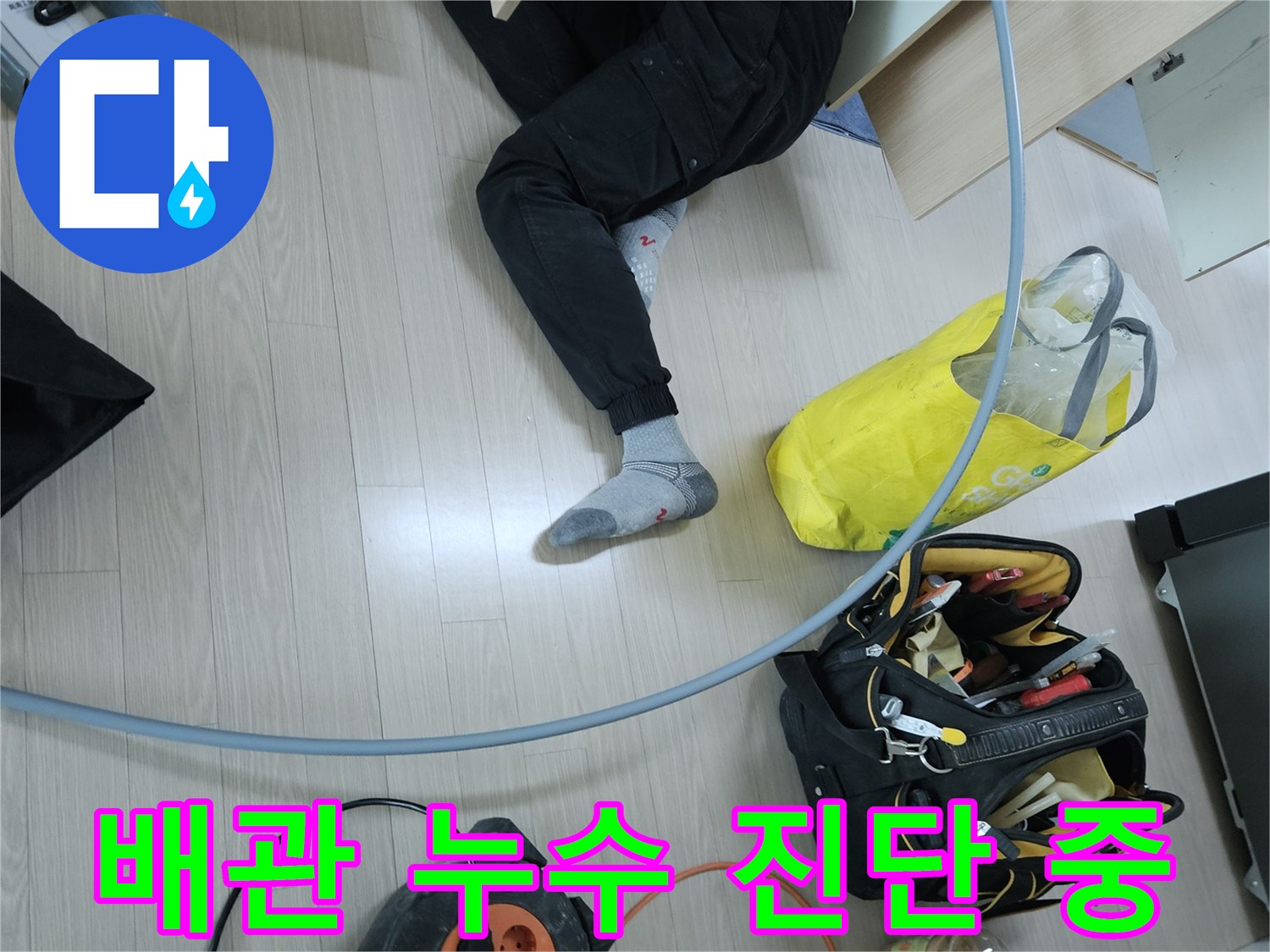 싱크대 하부장 아래쪽 좁은 공간에서 배관을 점검하는 모습입니다.