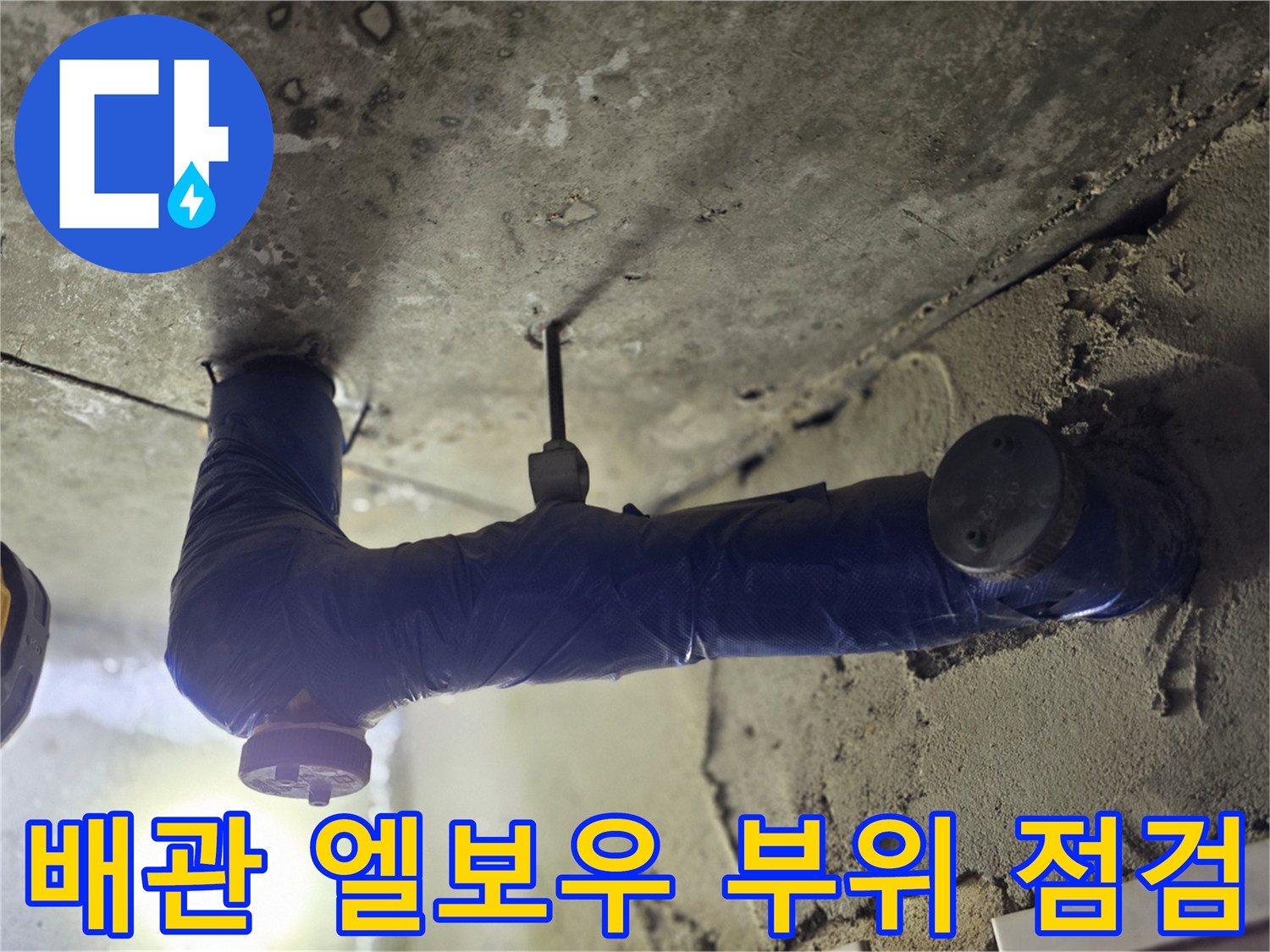 어두운 천장 내부의 파란색 배관 연결 부위를 비추는 조명 아래 모습