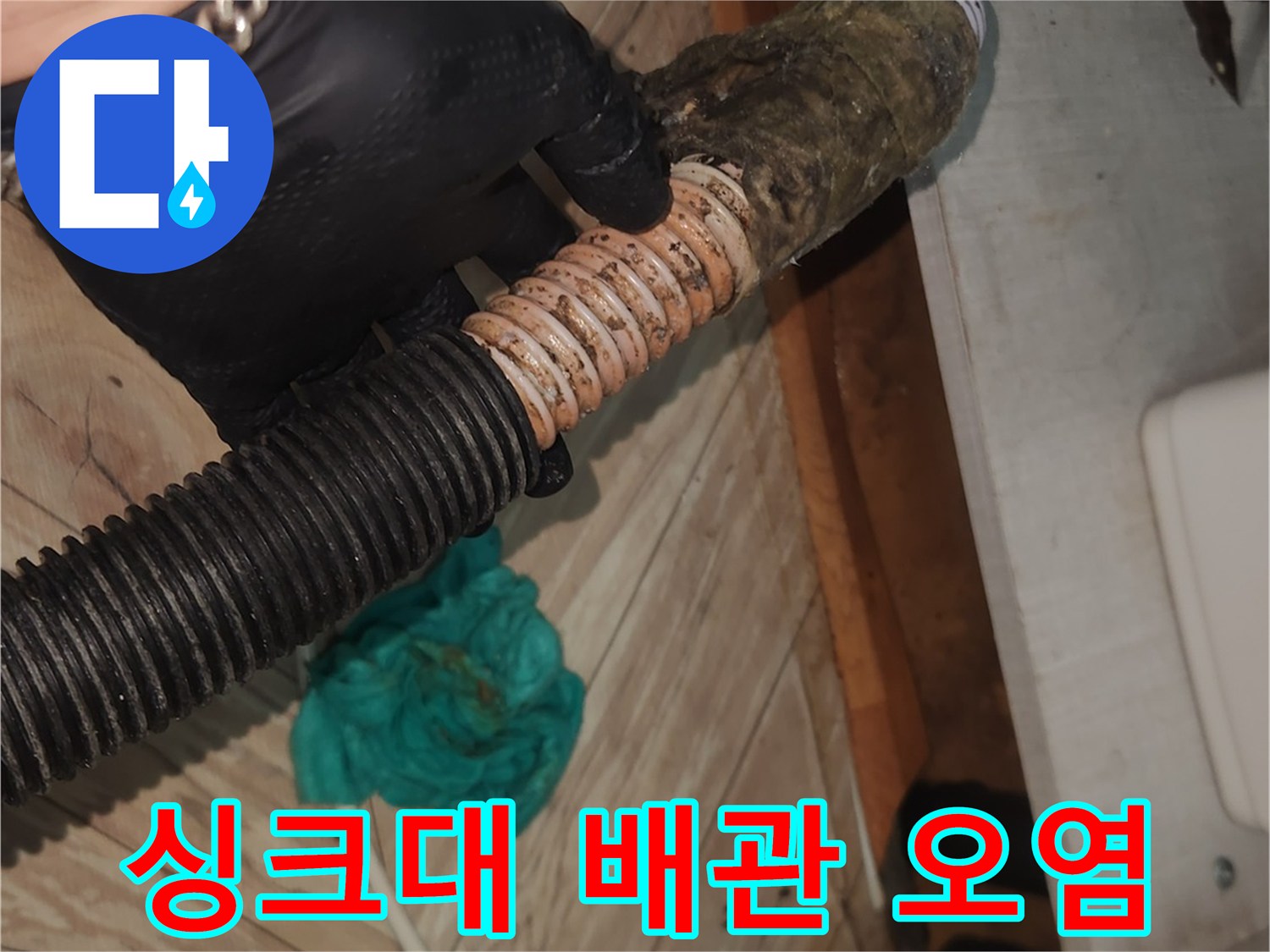 검은 장갑을 낀 손이-오랜 사용으로 찌꺼기가 쌓인 싱크대 배수 호스를-꼼꼼히 확인하며-석션 클리닝을 준비하는 모습