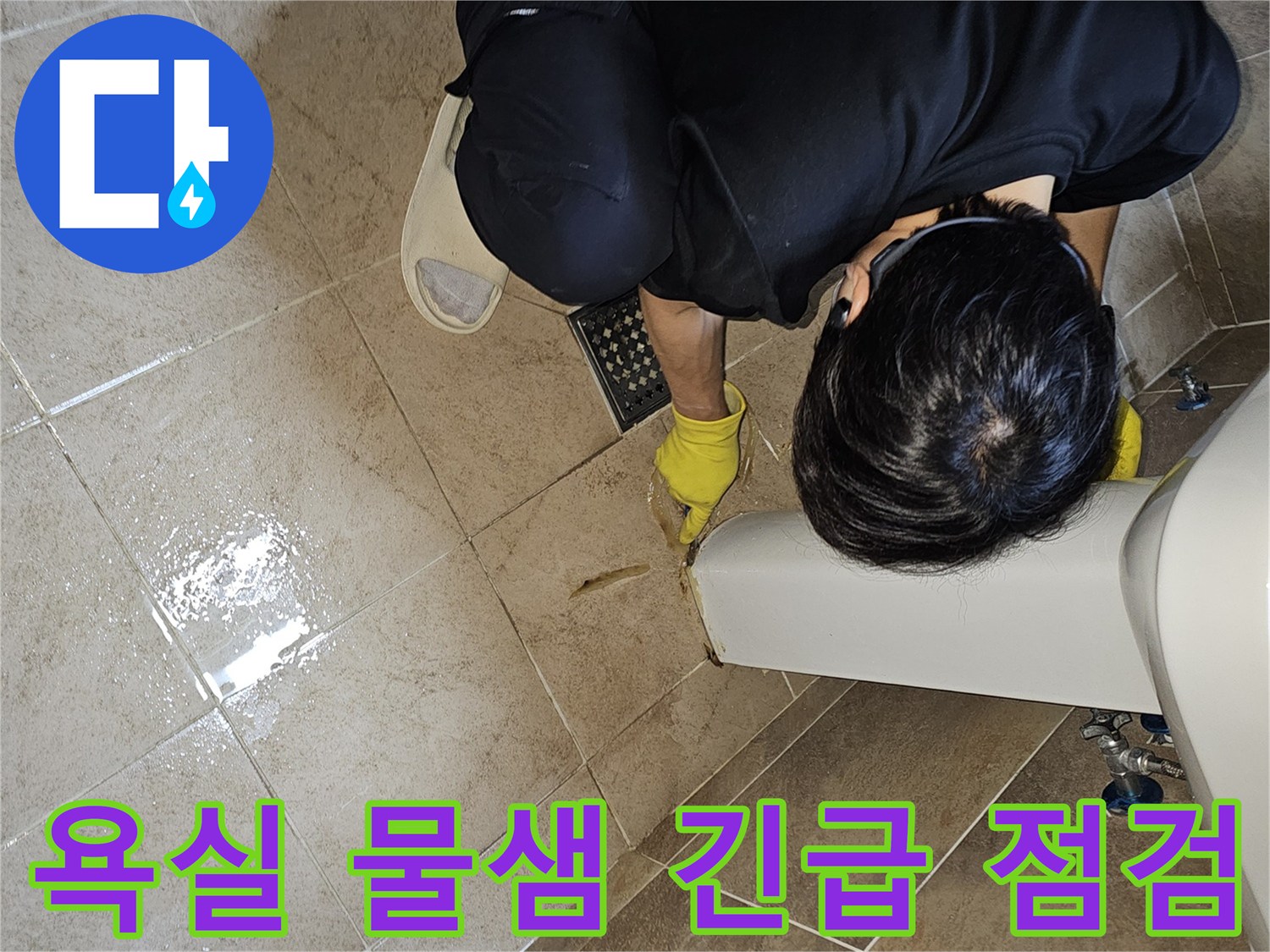 전문 엔지니어가-노란 장갑을 끼고-욕실 바닥의 젖은 타일과-세면대 하단부를-집중적으로 관찰하며-긴급 누수 지점을 파악하고 있습니다