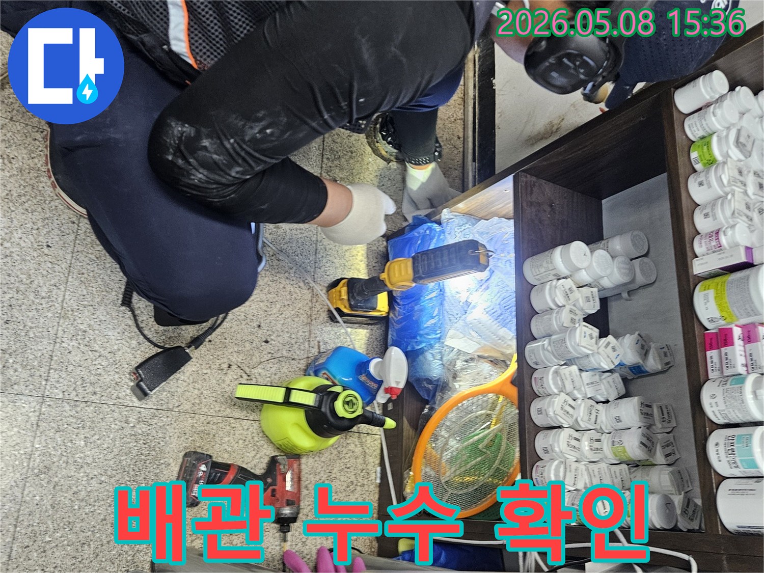 누수 전문가가-어두운 선반 밑에서-손전등을 비추며-배관 누수 여부를-확인하고 있습니다.