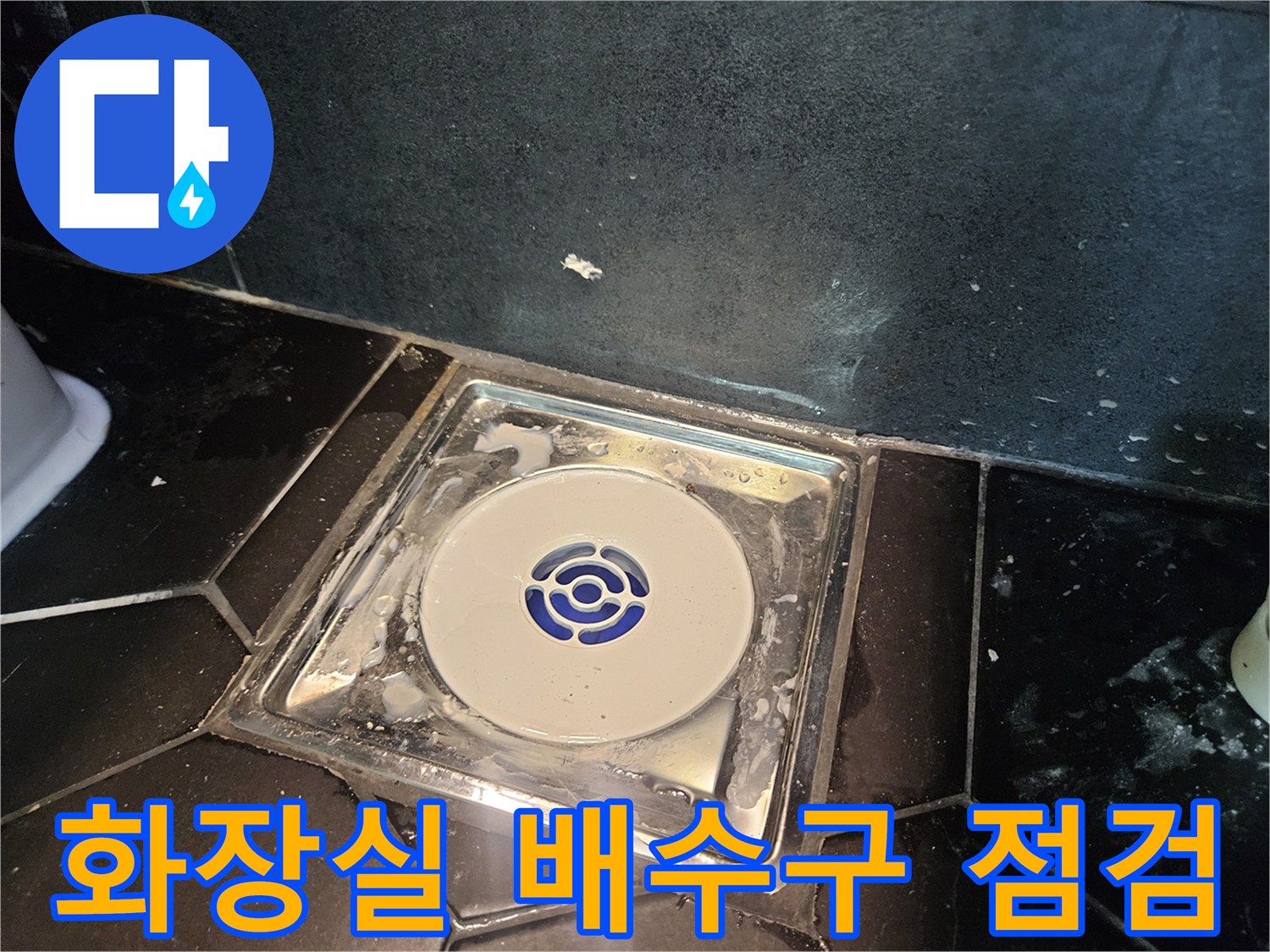 어두운 욕실 타일 사이의 하얀색 배수구 트랩 모습