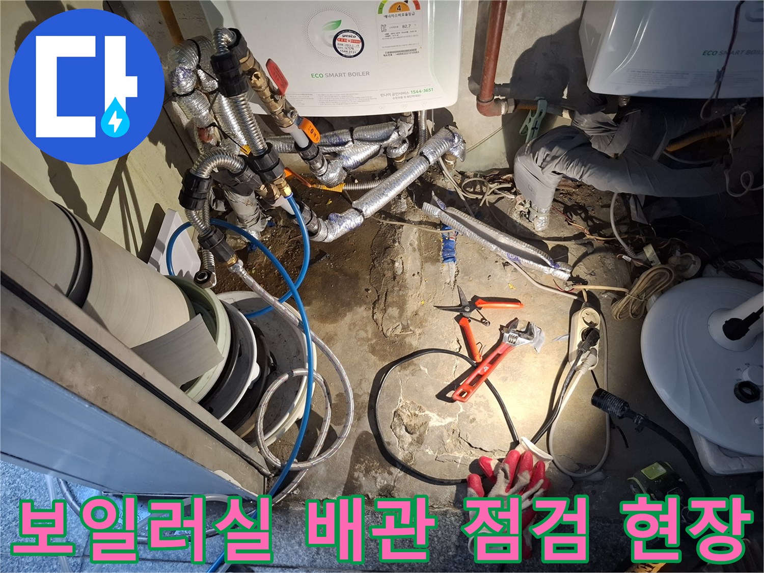 보일러 하단부 은색 배관과 작업용 펜치 및 장갑 배치