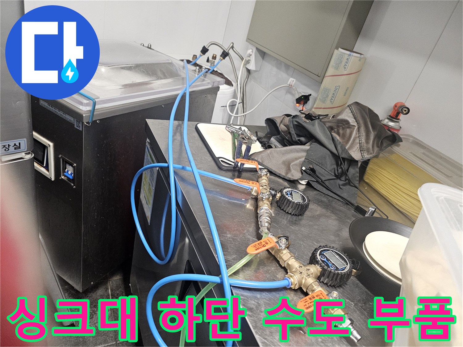 금속 밸브와 파란색 급수 호스가 연결된 싱크대 내부 모습입니다.