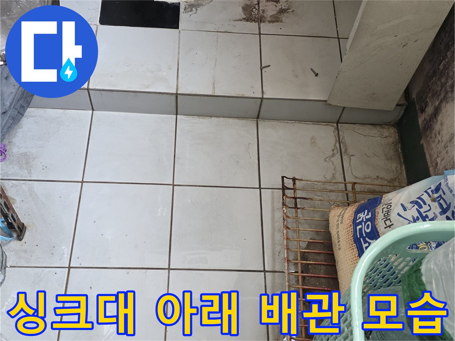 파란색 배관이 지나가는 싱크대 하단 타일 벽면 사진