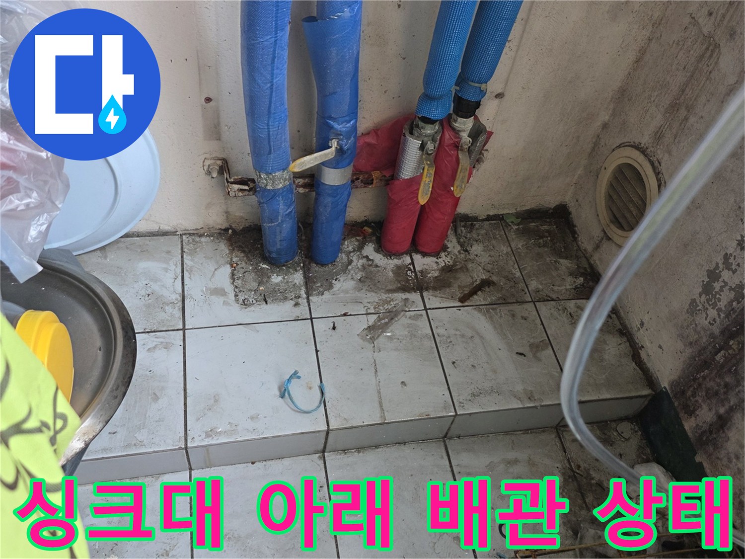 파란색과 빨간색 배관이 연결된 싱크대 밑 바닥 타일 부위