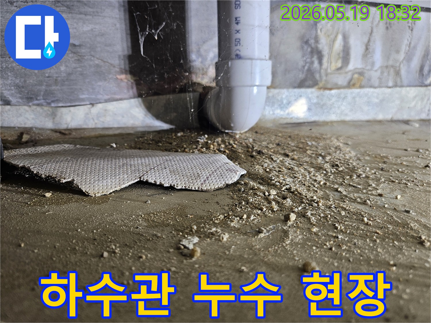 누수 공사 전-배관 주변의 물기와 흙먼지로-오염된 바닥 상태를 기록한 사진