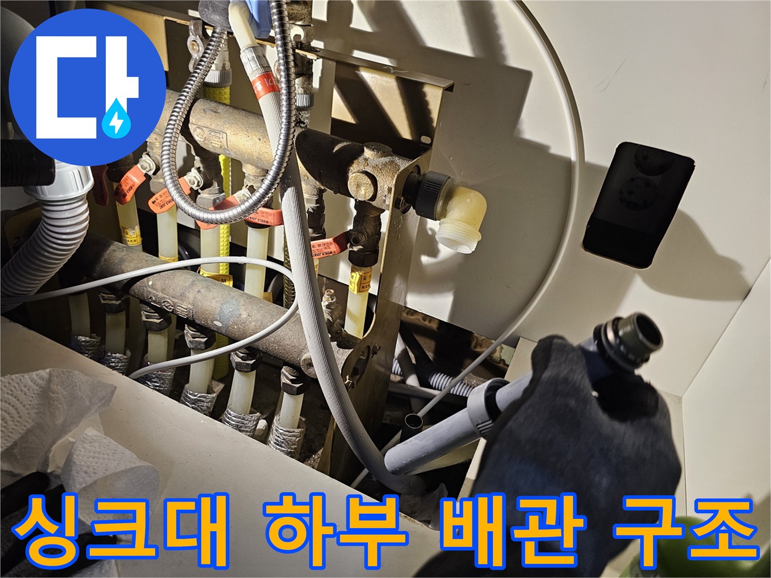 싱크대 아래 복잡한 구조의 배관과 연결 소켓들을 촬영한 사진