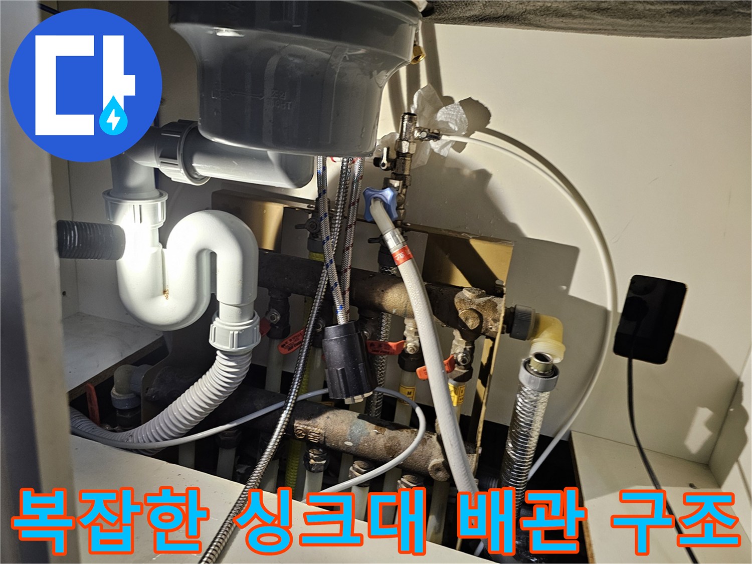 싱크대 아래쪽의 다양한 급수 및 배수 배관 연결 상태