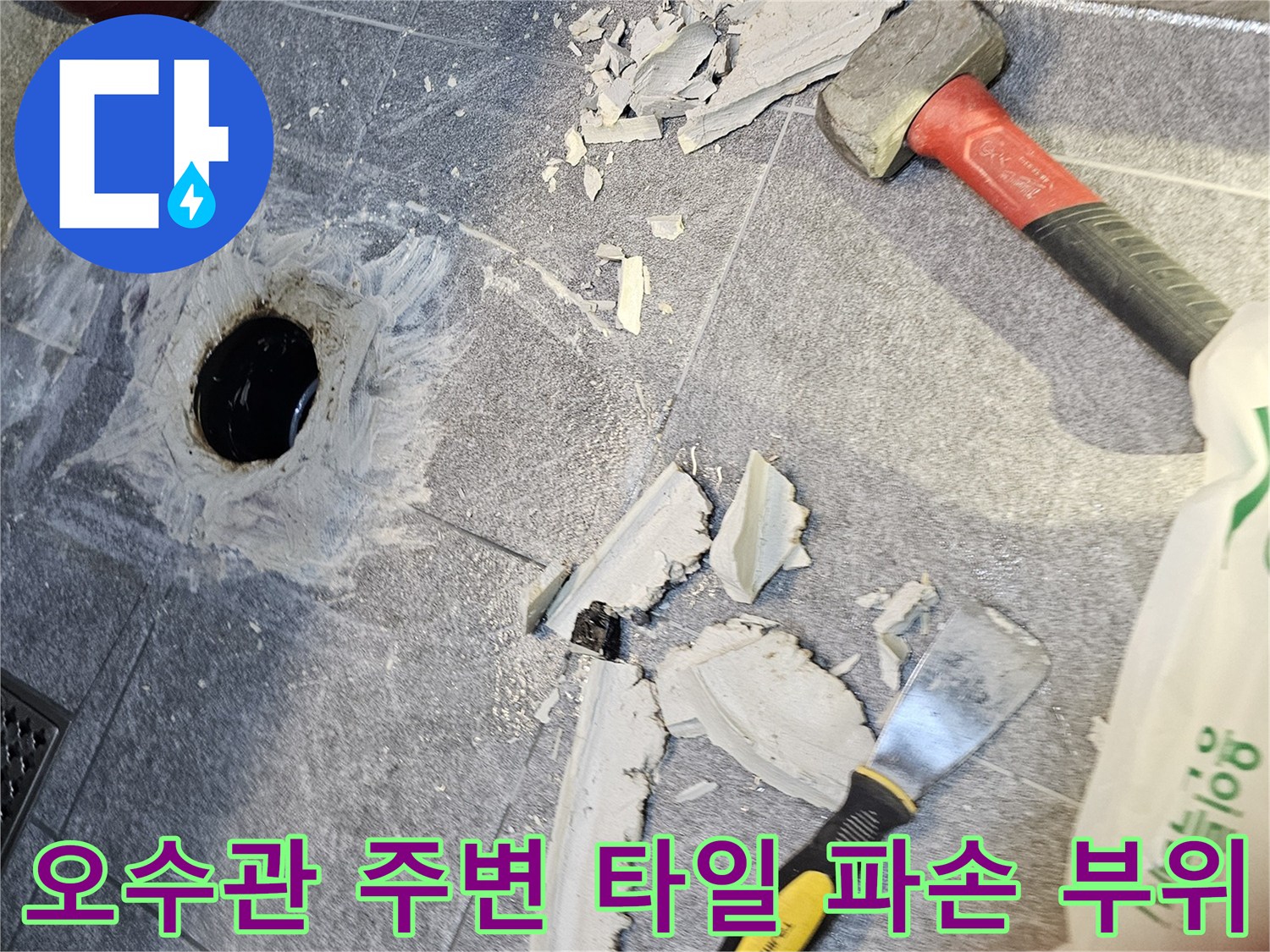 망치와 헤라를 사용하여 오수관 주변의 깨진 타일을 제거하는 모습