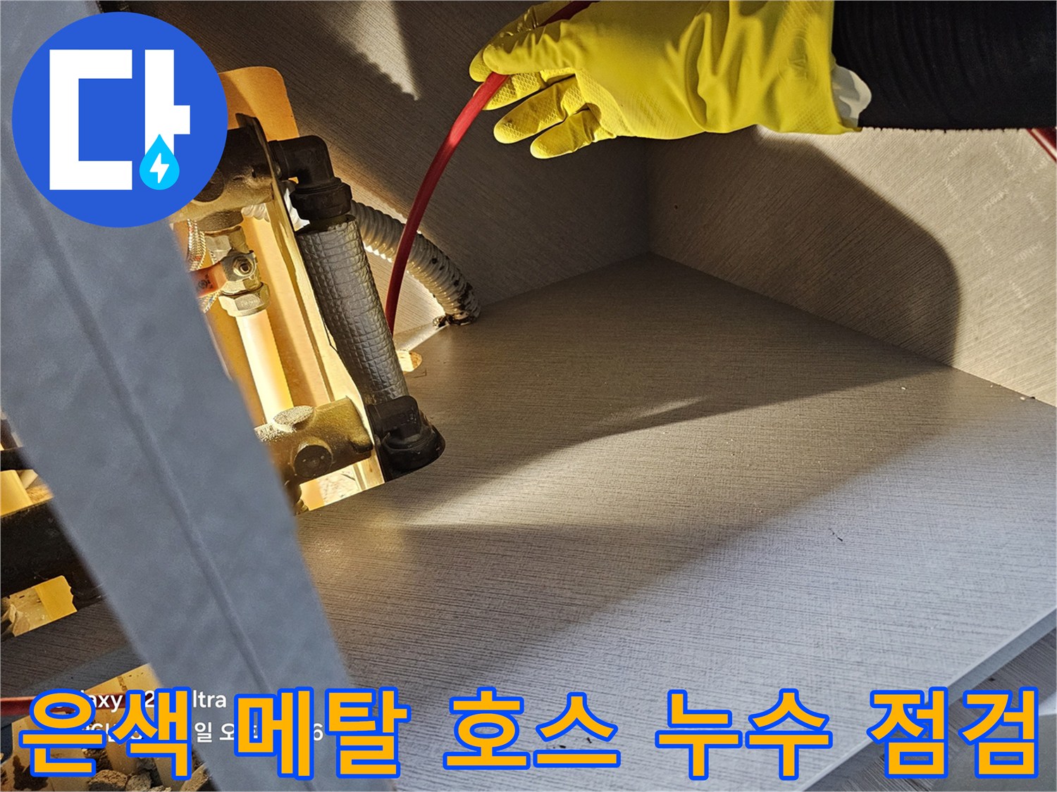 노란 장갑을 낀 작업자의 손이 - 싱크대 하부 은색 배관을 만지는 사진
